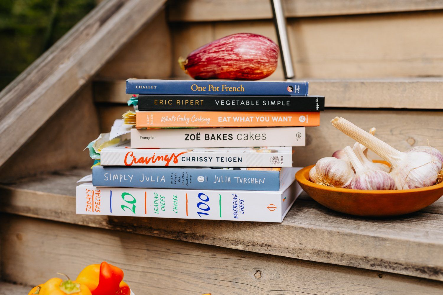 A stack of books sitting on top of a wooden staircase next to a bowl of garlic.
