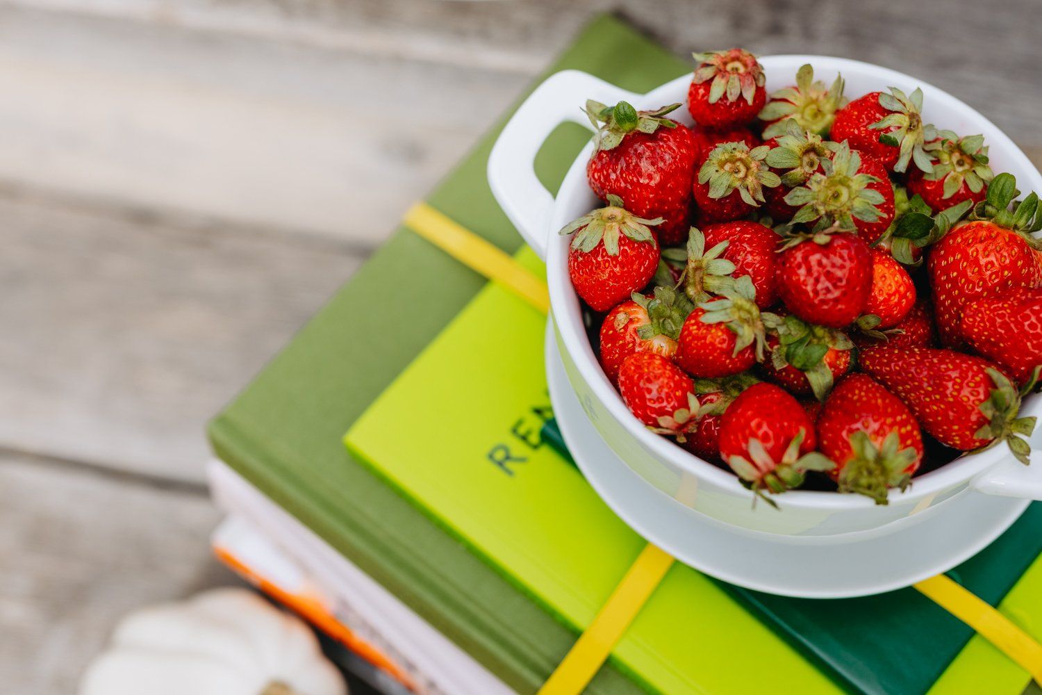 A bowl of strawberries is sitting on top of a stack of books.