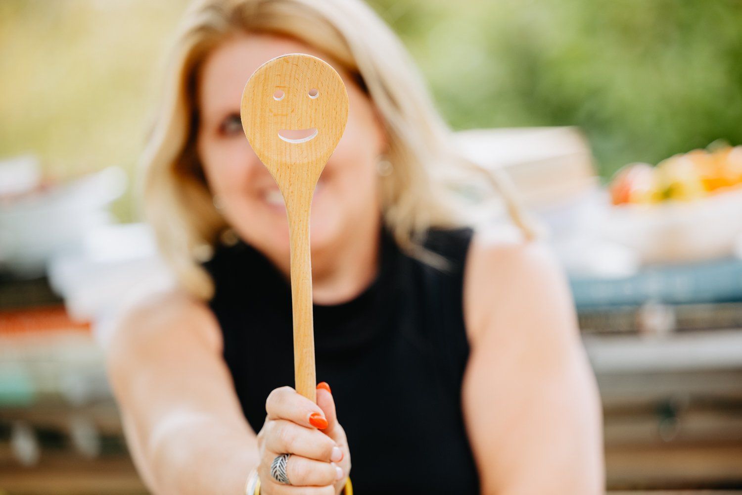 A woman is holding a wooden spoon with a smiley face on it.