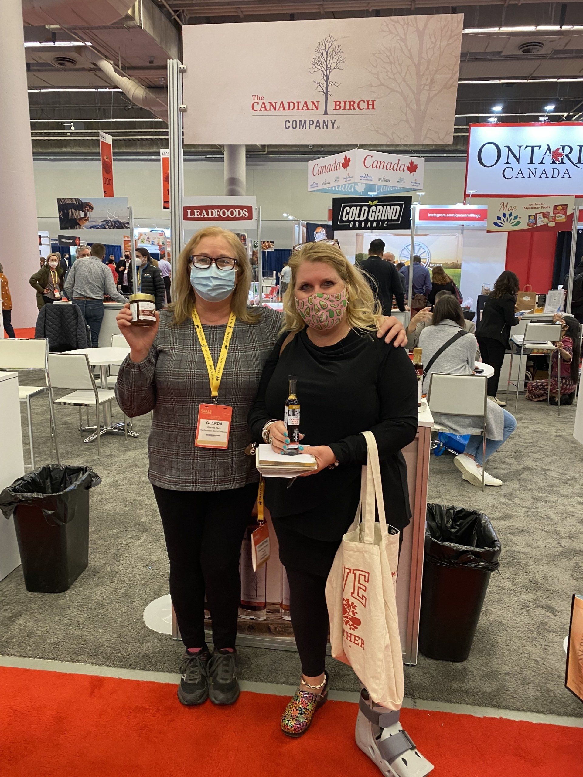 Two women wearing face masks are posing for a picture at a convention.