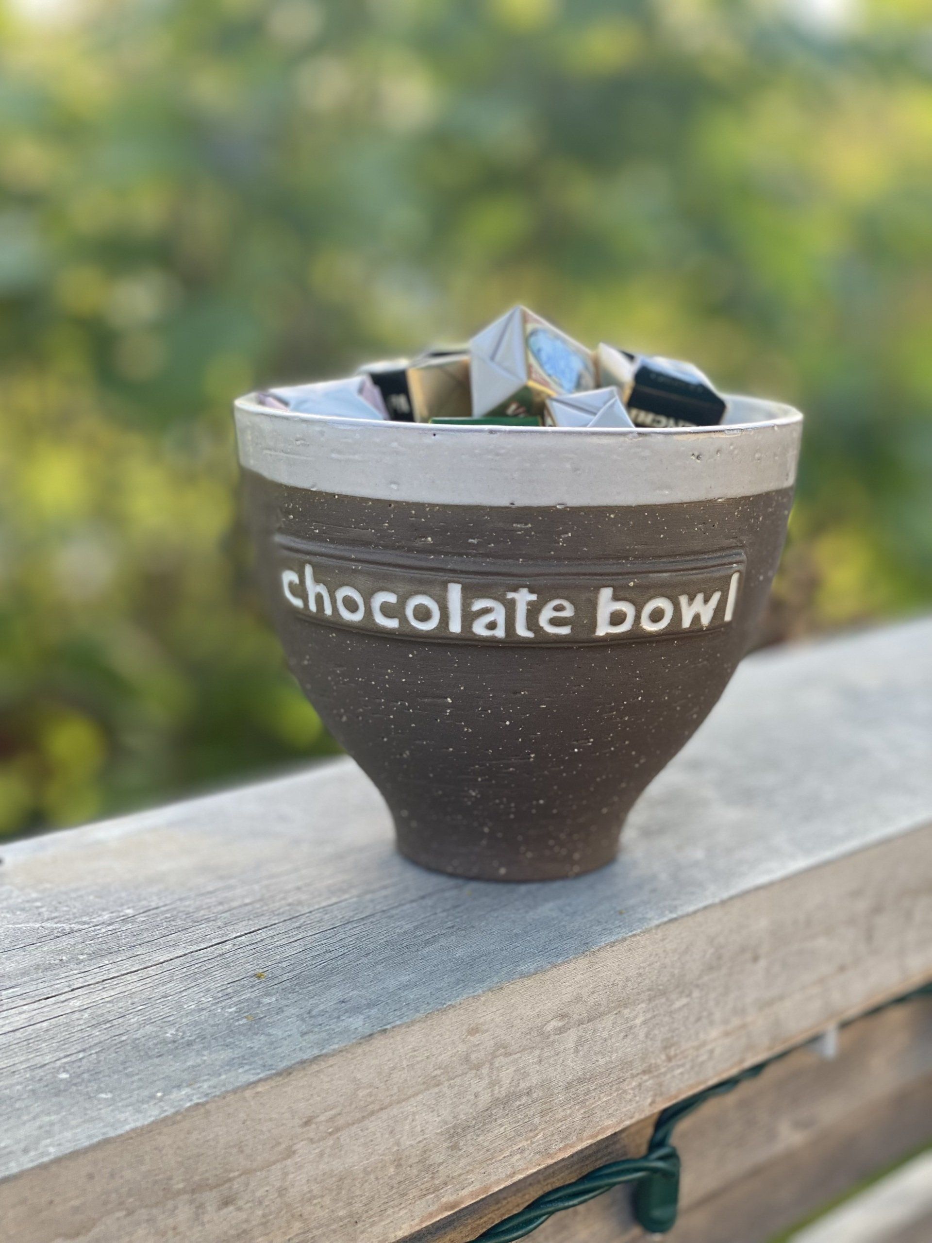 A chocolate bowl is sitting on a wooden railing.