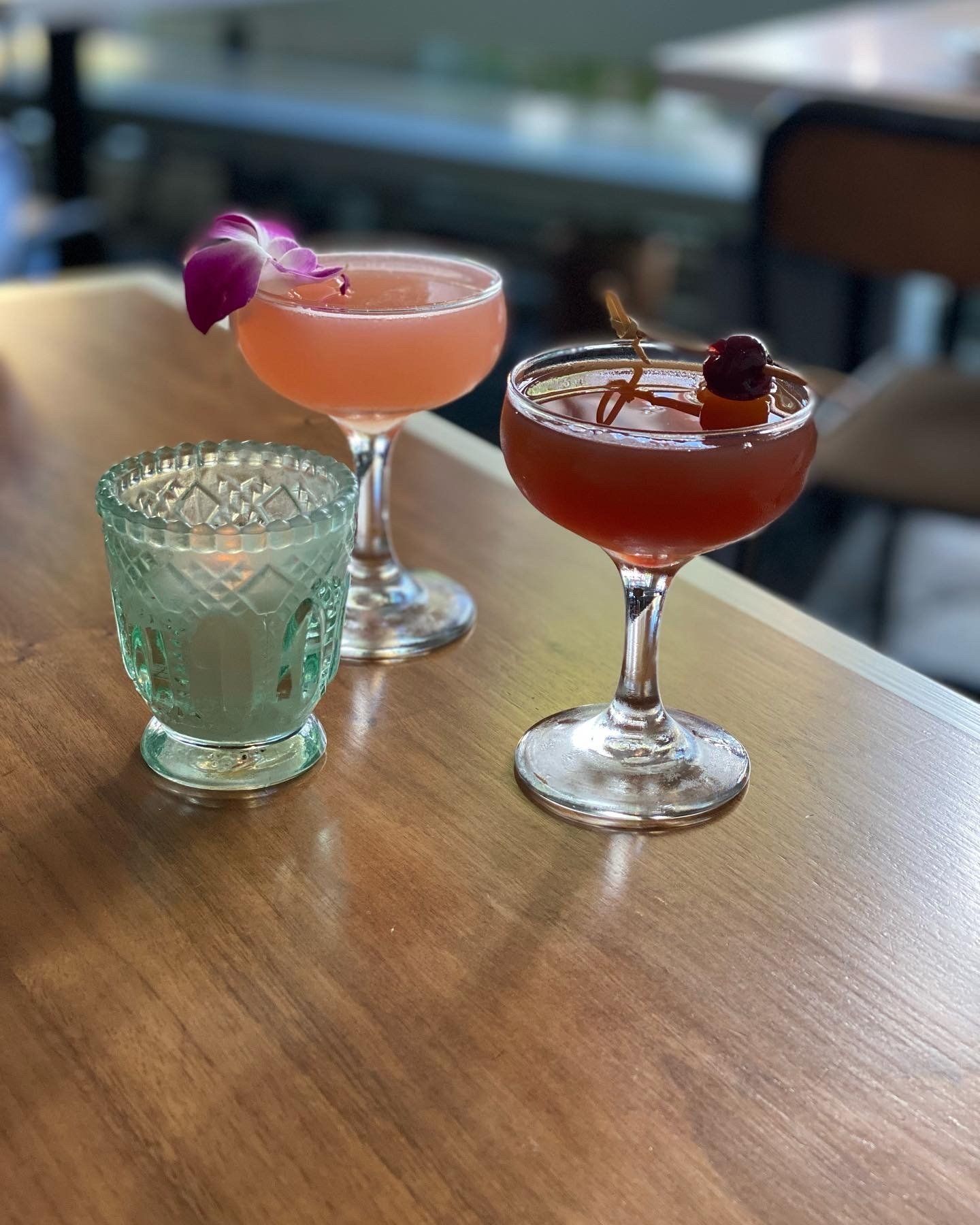 Three cocktails are sitting on a wooden table.