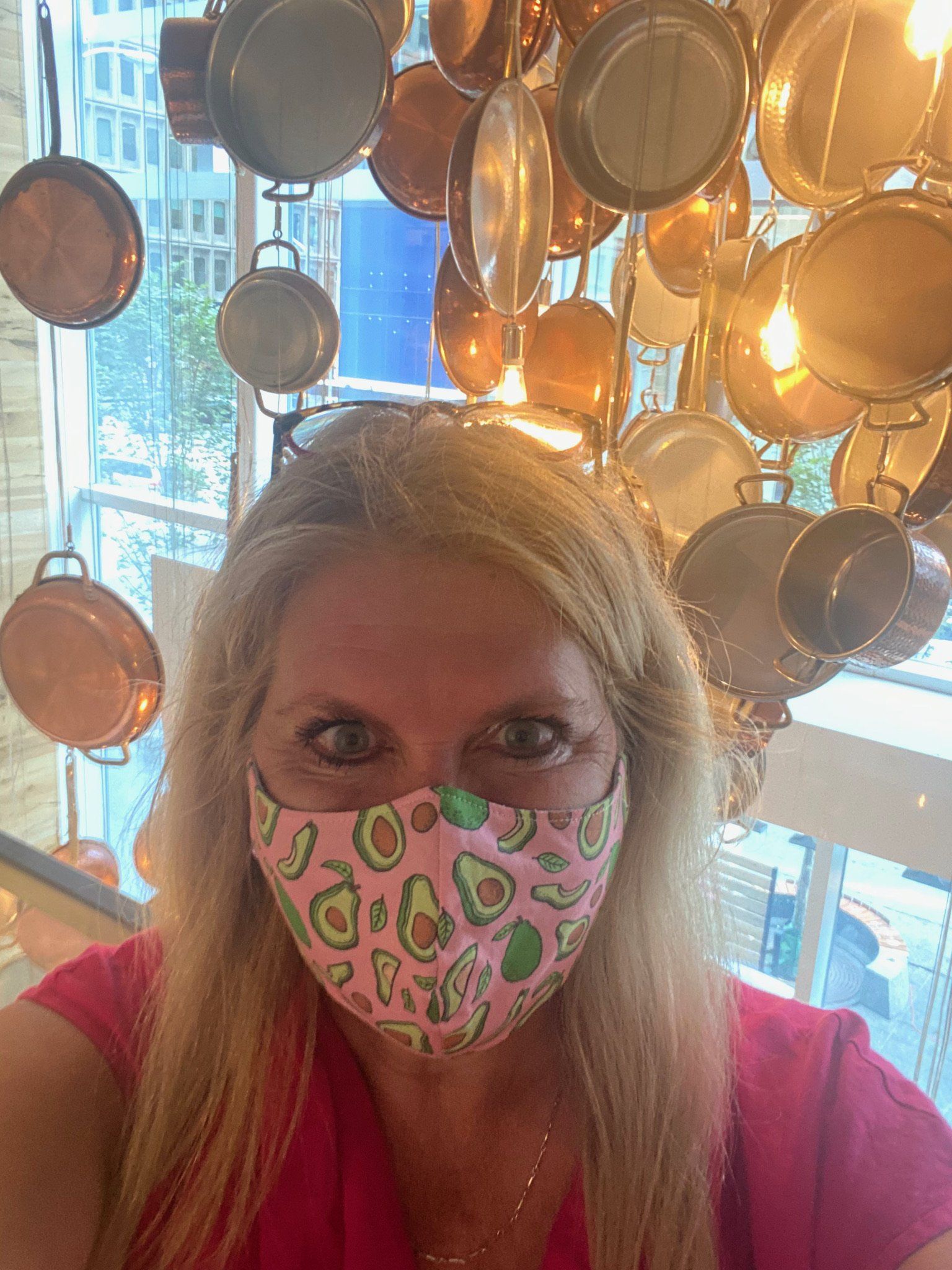 A woman wearing a face mask is standing in front of a wall of pots and pans.