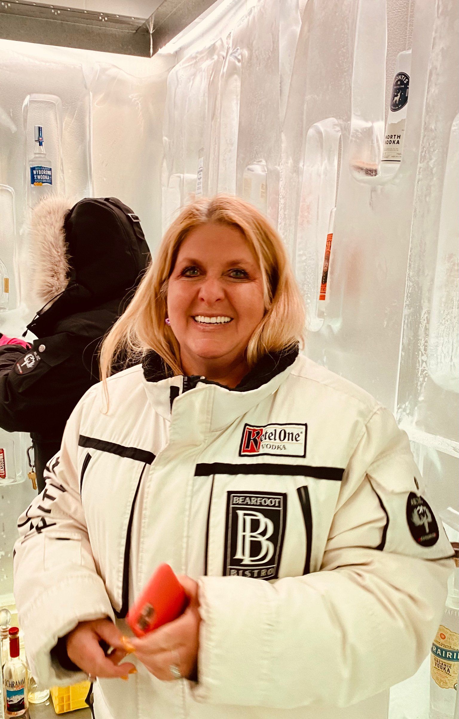 A woman in a white jacket is standing in front of a wall of ice.