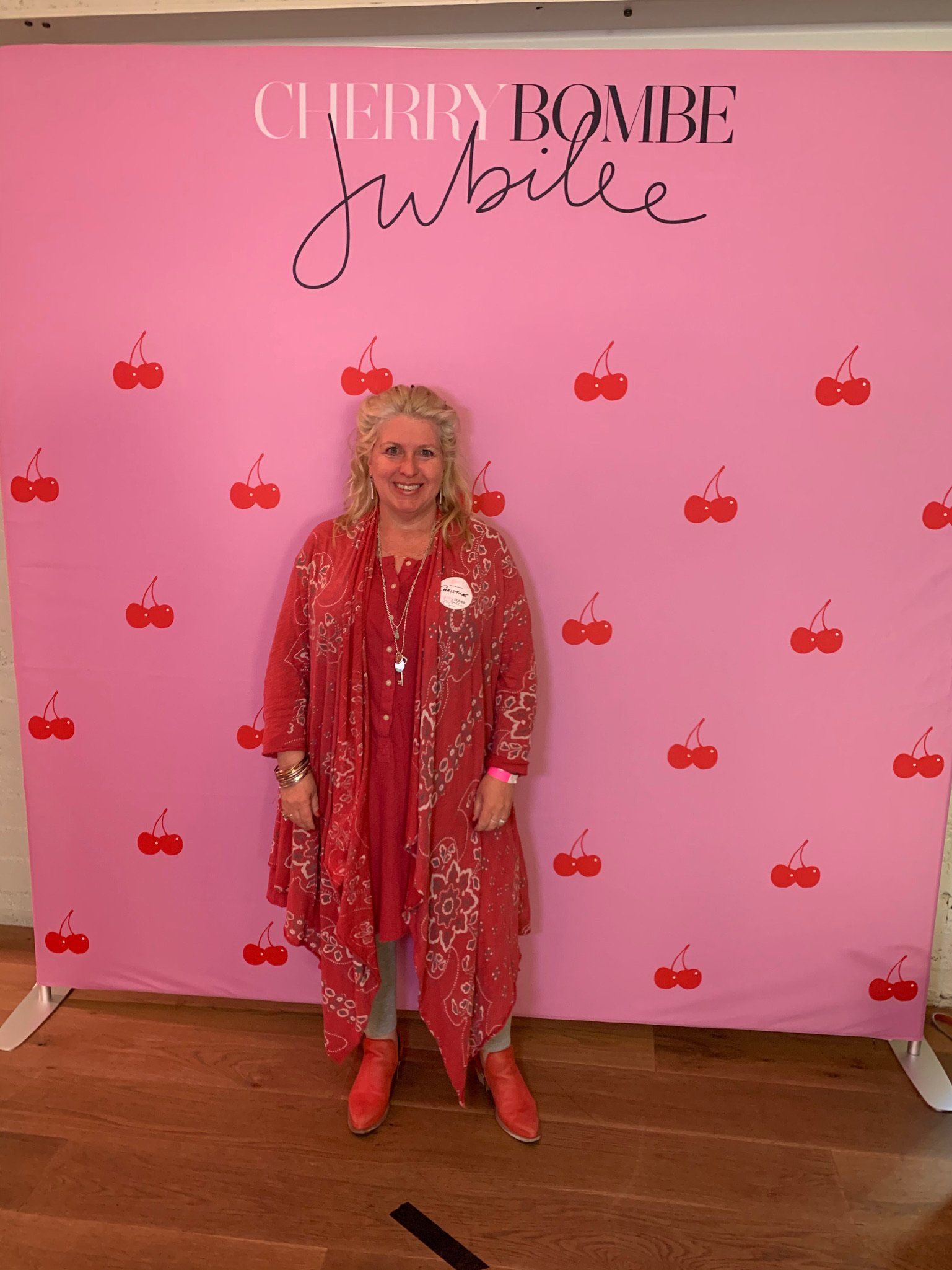 A woman in a red dress is standing in front of a pink wall with cherries on it