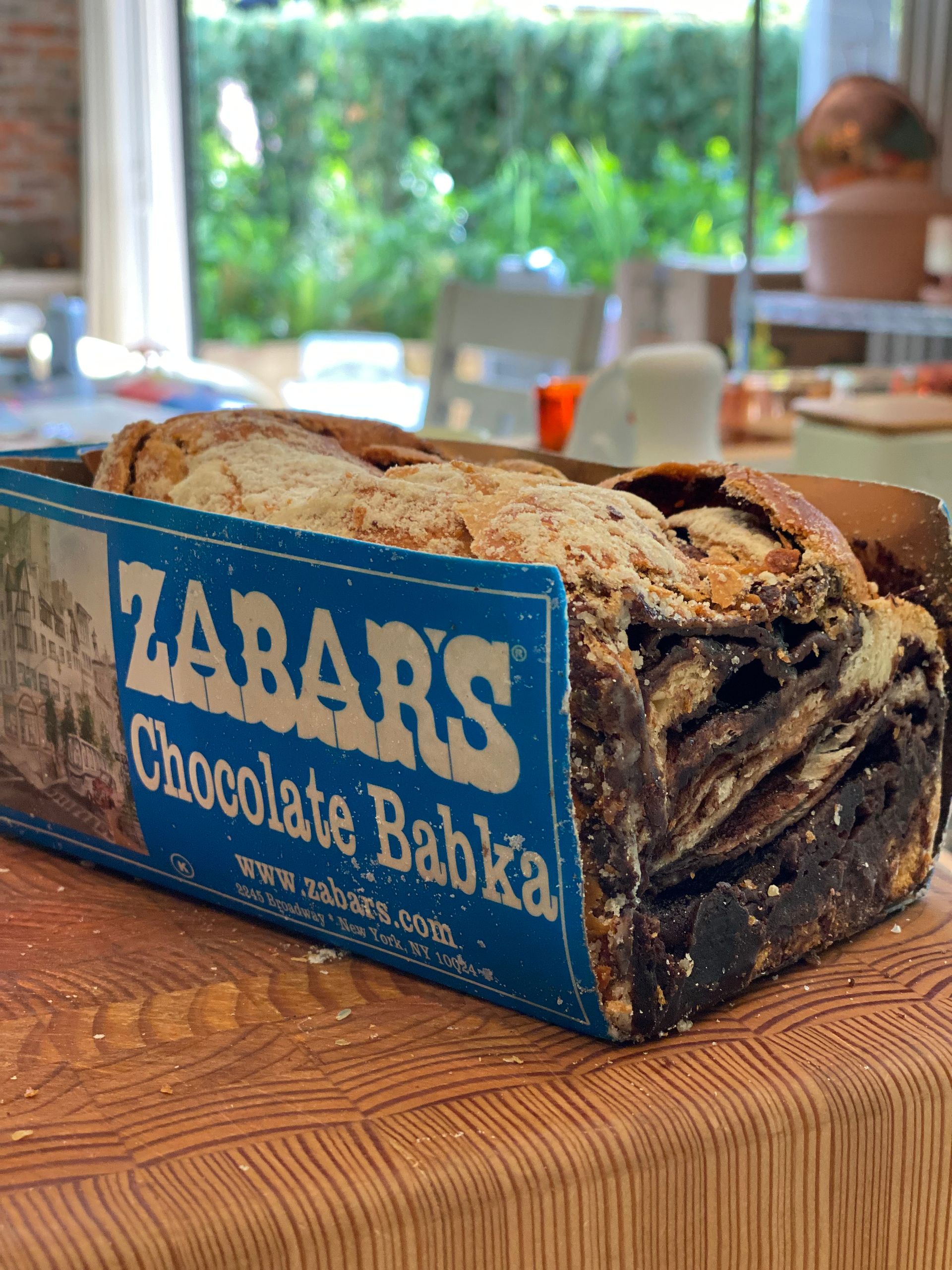 A loaf of chocolate babka is in a box on a wooden table.