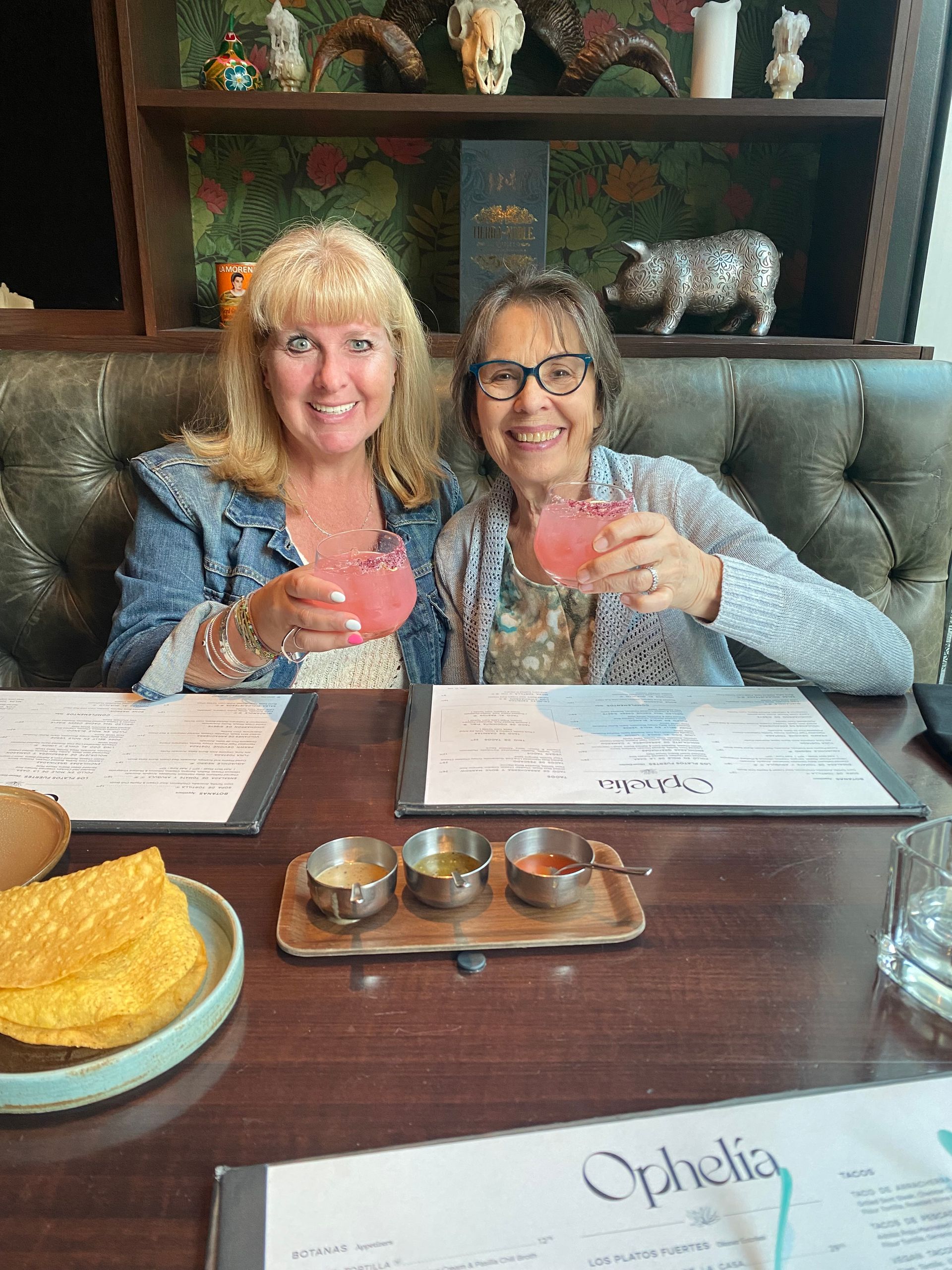 Two women are sitting at a table in a restaurant holding drinks.