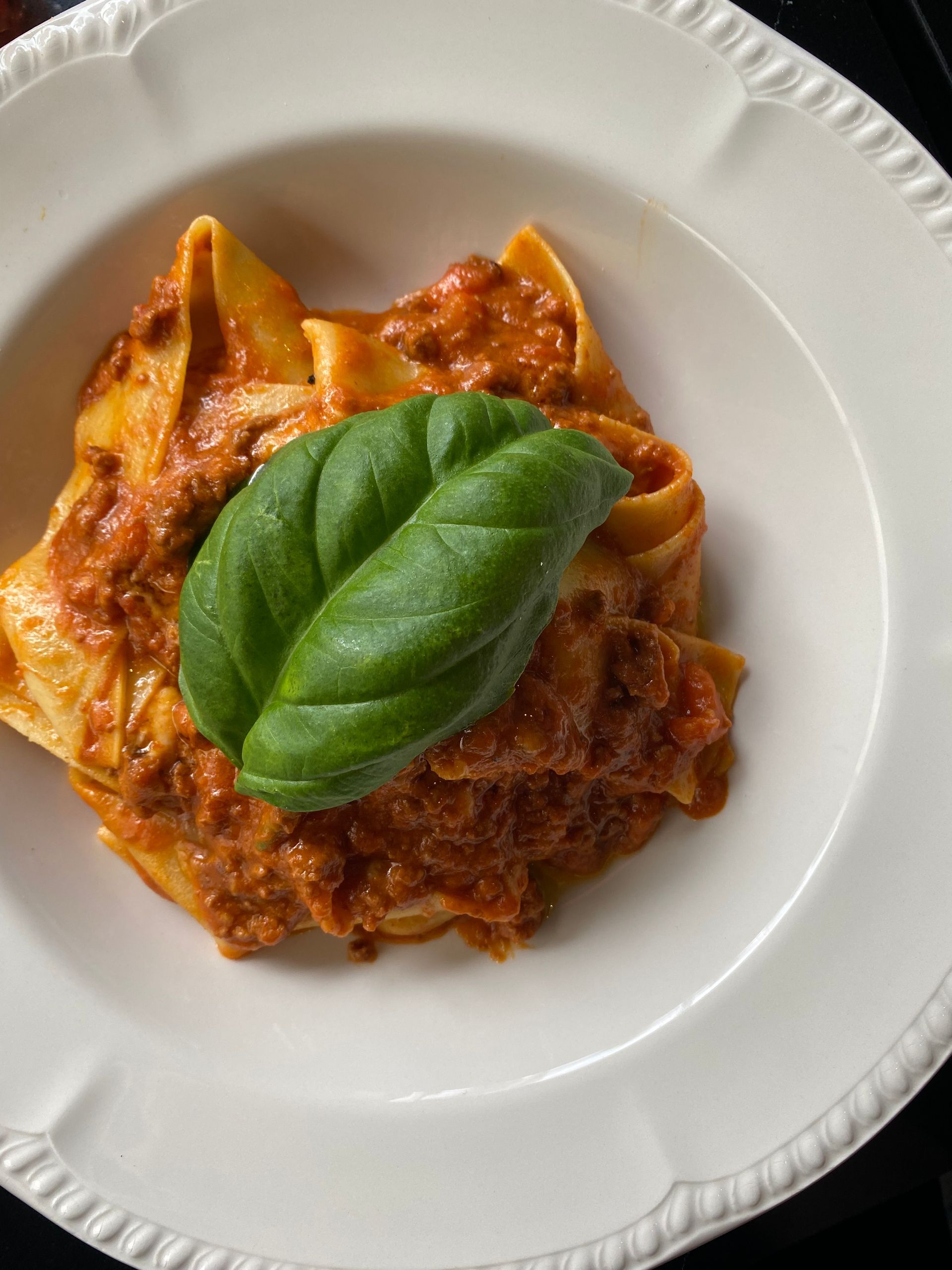 A white plate topped with pasta and sauce with a basil leaf on top.