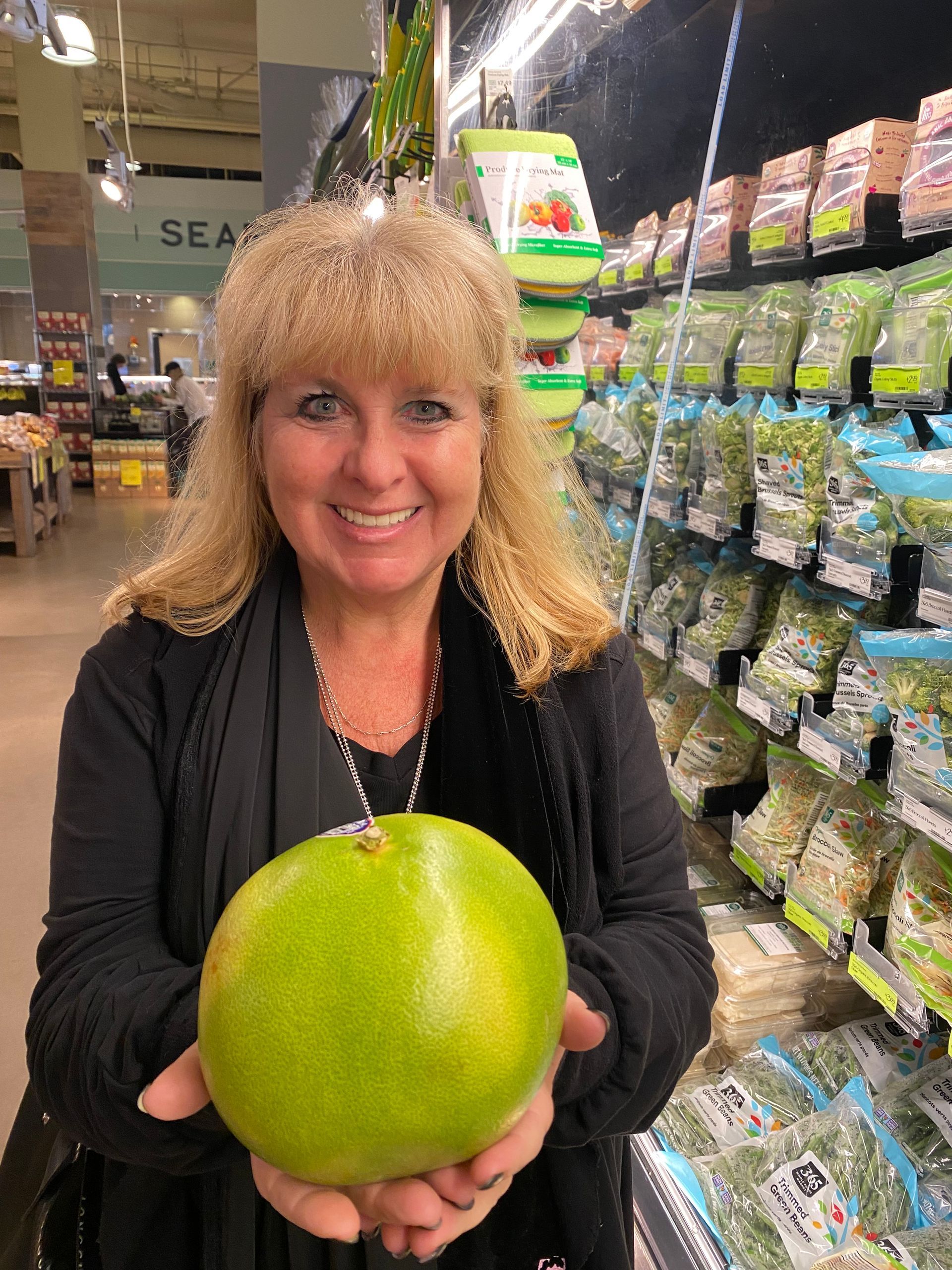 A woman is holding a green pomelo in a grocery store.