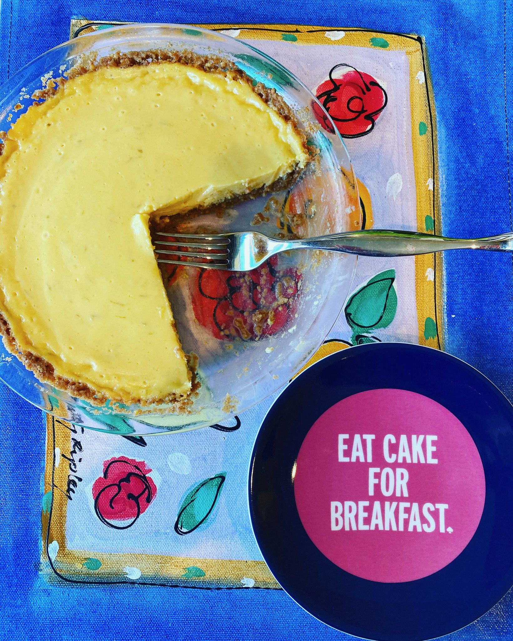 A pie with a slice taken out of it next to a plate that says eat cake for breakfast