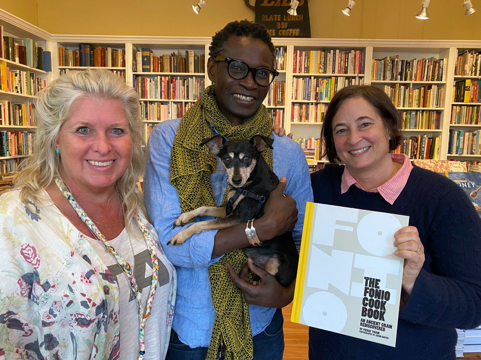 A man is holding a dog and two women are holding a book.