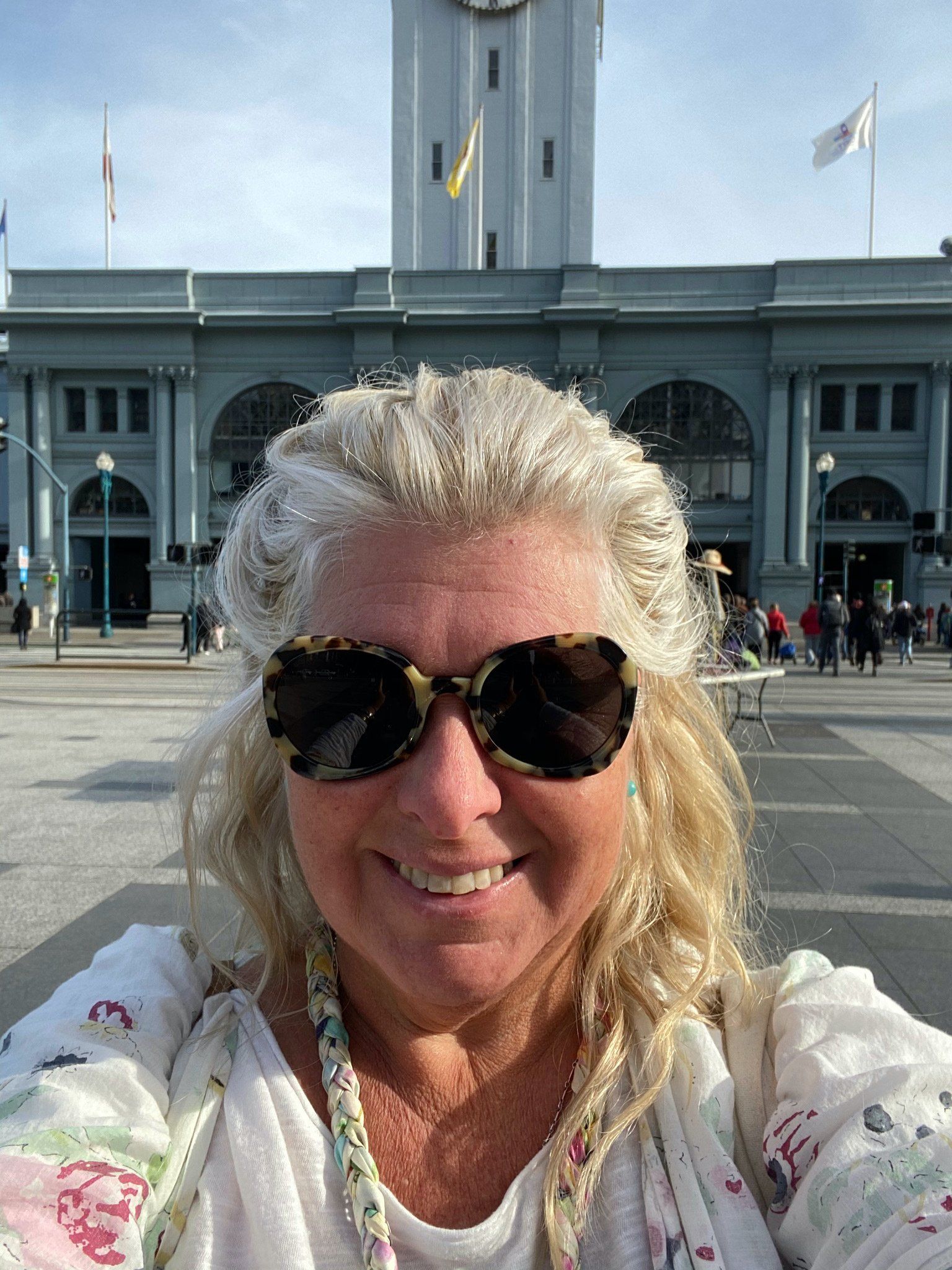 A woman wearing sunglasses is taking a selfie in front of a building.