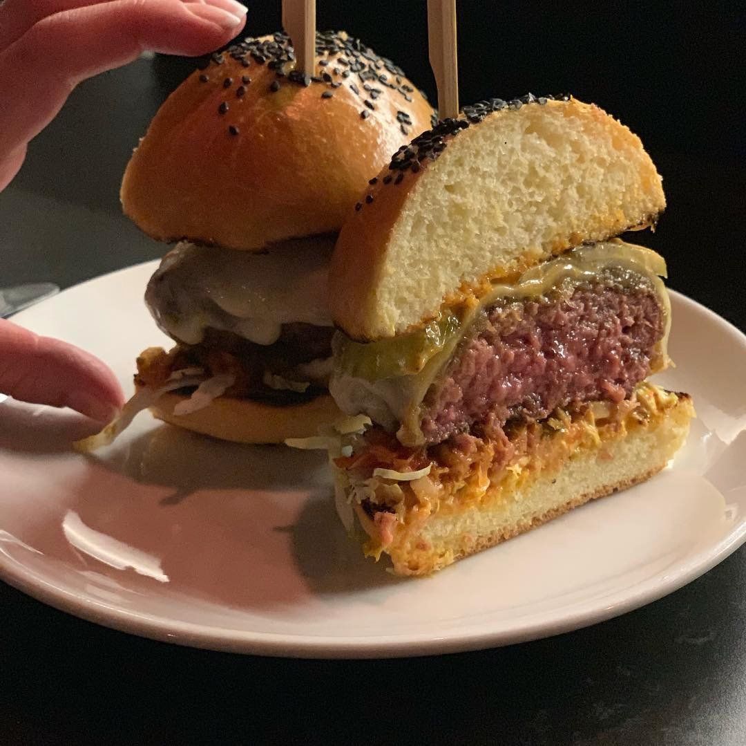 A white plate topped with two hamburgers with toothpicks in them