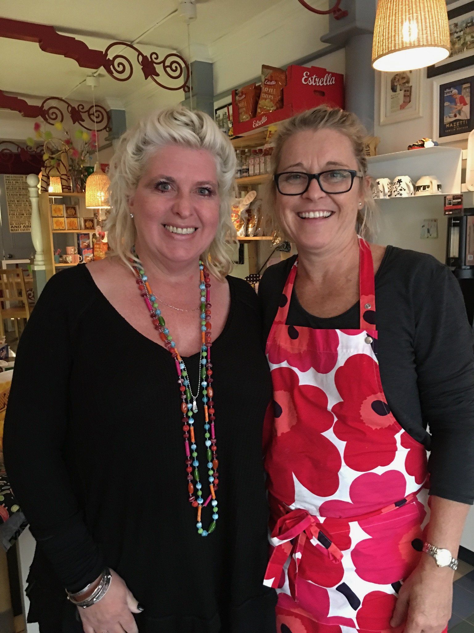 Two women wearing aprons are posing for a picture in a store.