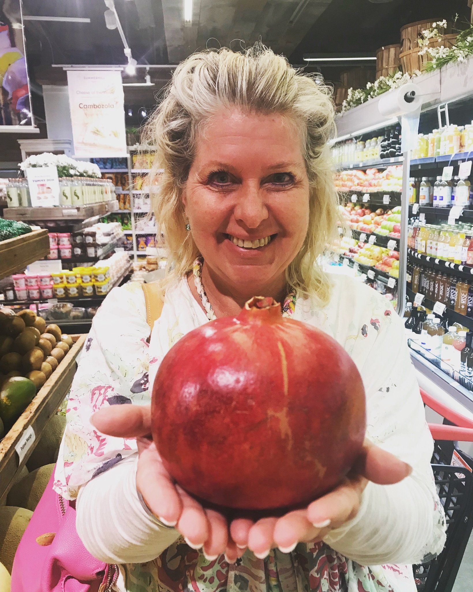 A woman is holding a pomegranate in her hands in a grocery store.