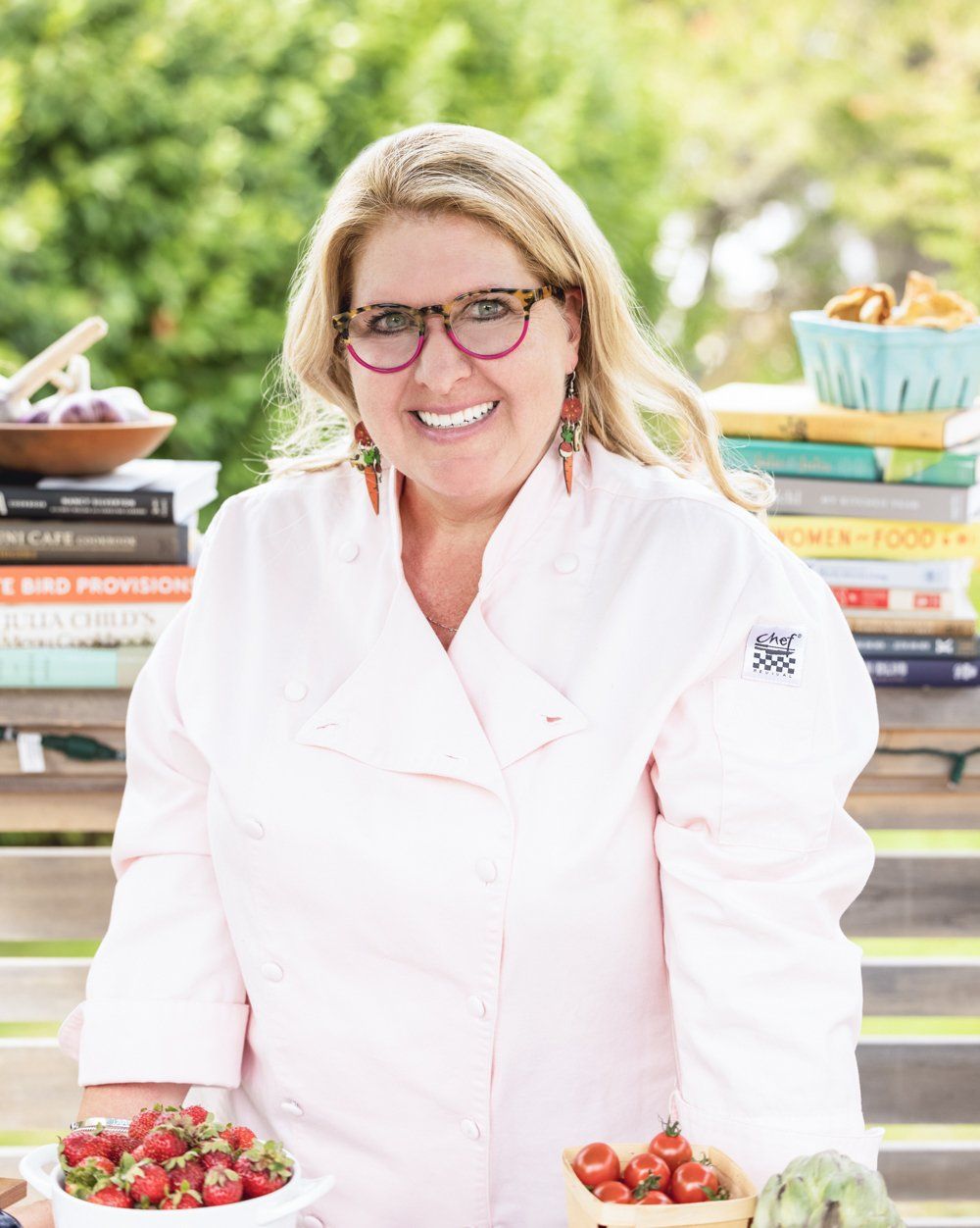 A woman in a chef 's coat is holding a bowl of strawberries.