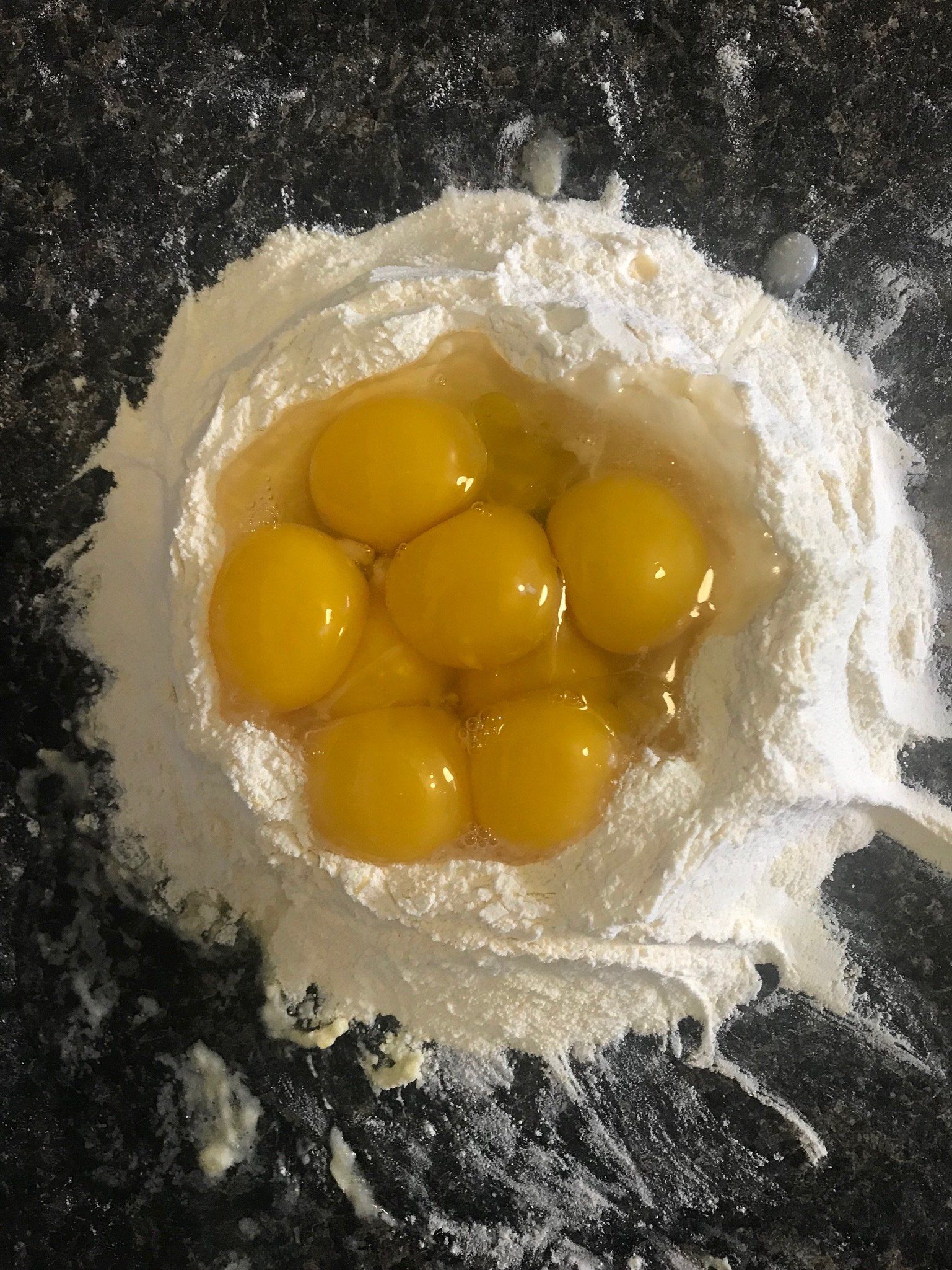 A pile of flour with eggs in it on a table.
