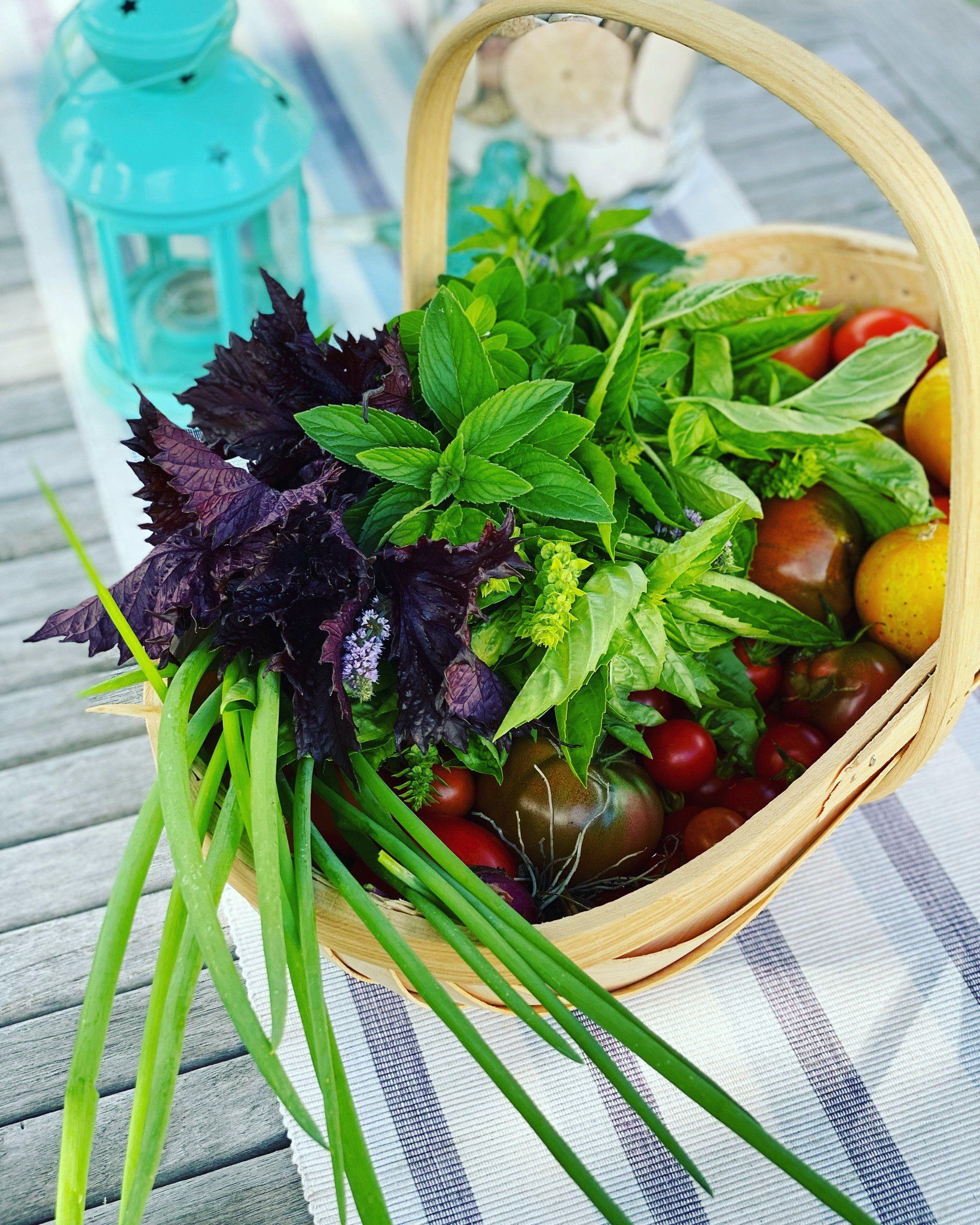 A basket filled with vegetables is on a table next to a blue lantern.