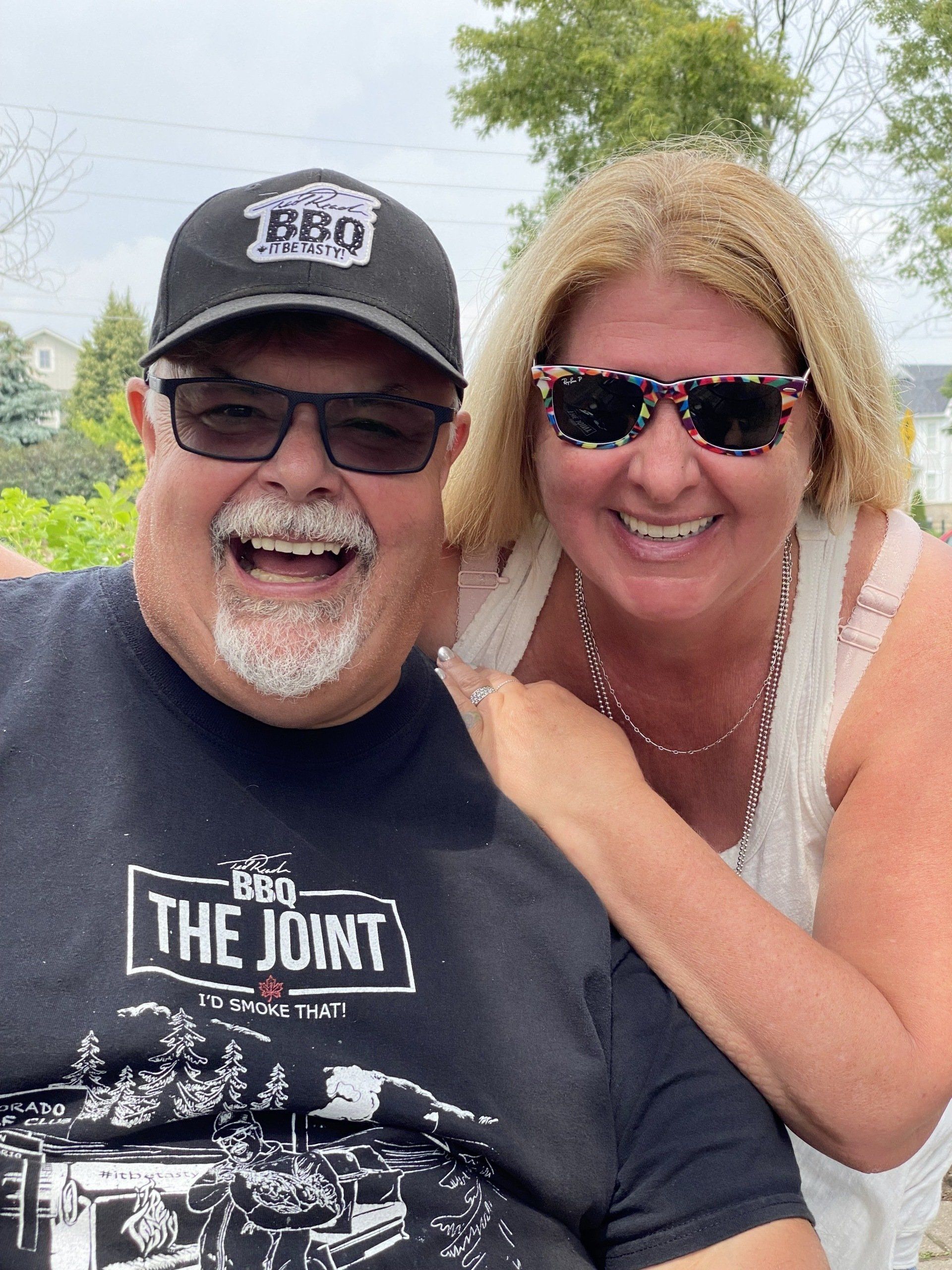 A man and a woman are posing for a picture . the man is wearing a shirt that says the joint.