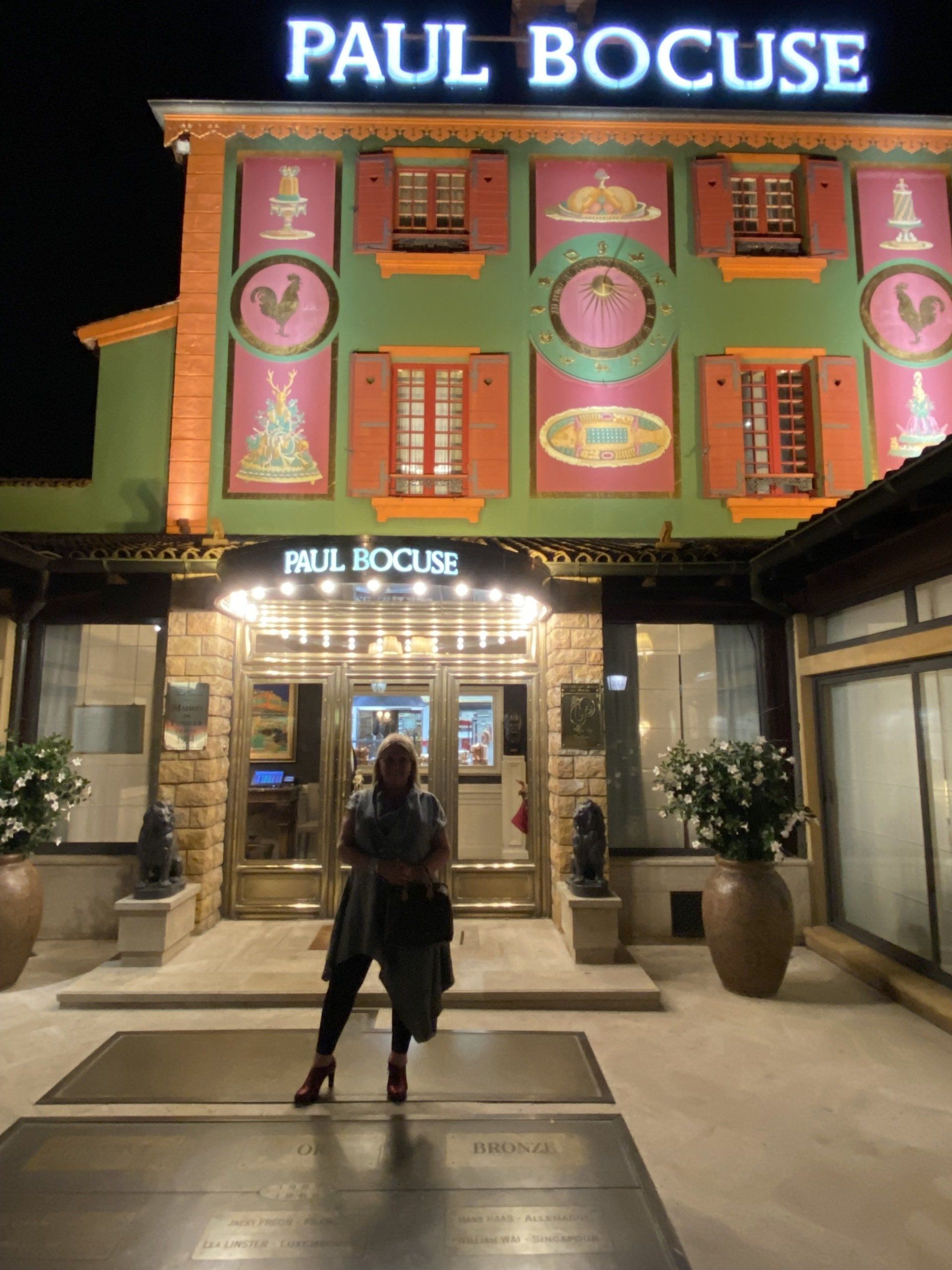 A woman is standing in front of a paul bocuse restaurant