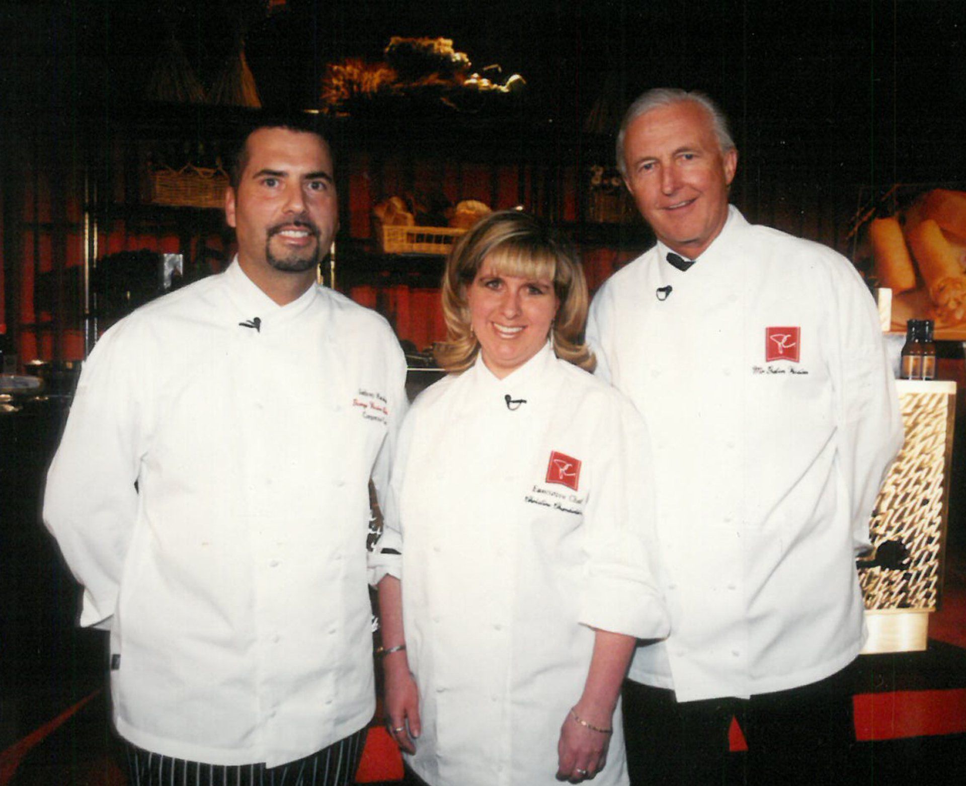 Three chefs are posing for a picture and one of them has a red r on his shirt