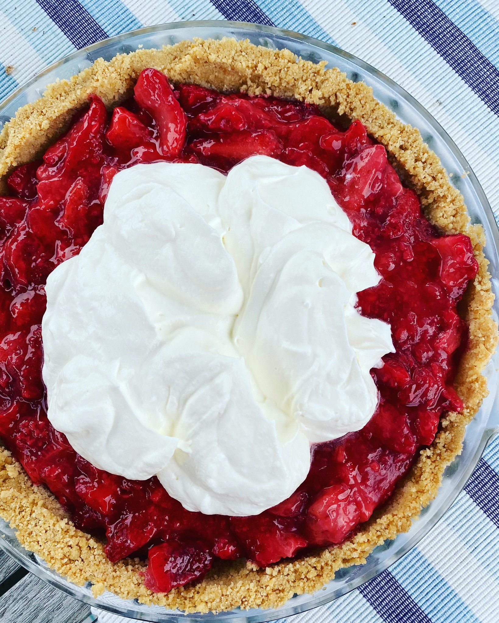 A strawberry pie with whipped cream on top is sitting on a table.