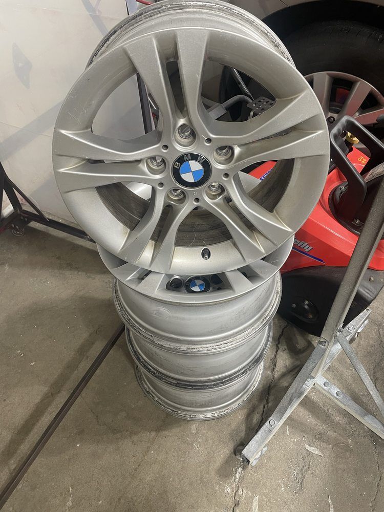 Four silver BMW car rims stacked on top of each other, in a garage setting.