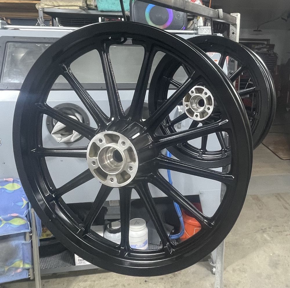Two black motorcycle wheels with spokes, in a workshop setting.