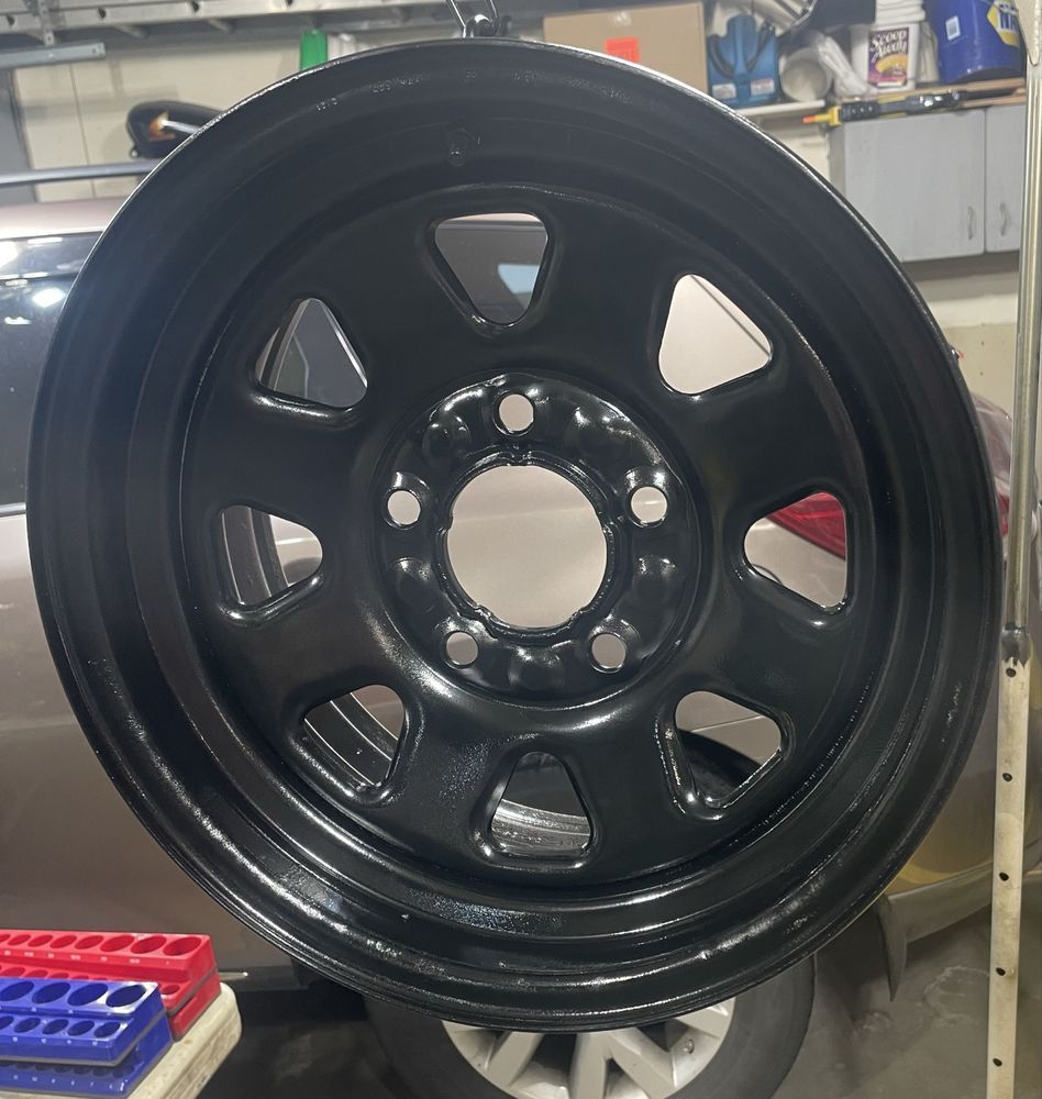 Black steel wheel rim, freshly painted, in a garage setting.