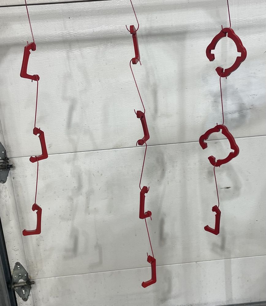 Red painted metal parts hanging from wires in front of a white garage door.