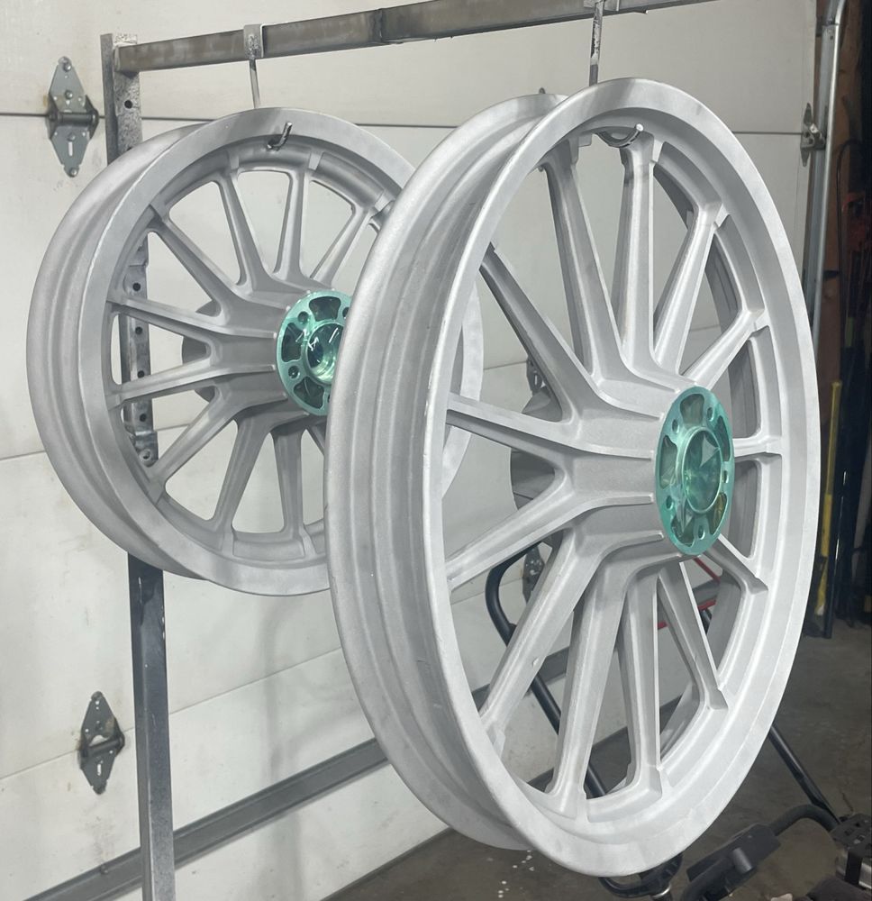 Two silver motorcycle wheels hanging on a rack; teal hubs, garage setting.