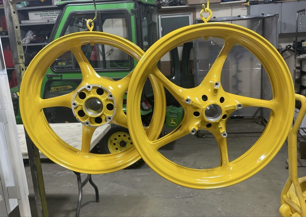 Two yellow motorcycle wheels hanging in a workshop, with a green tractor in the background.