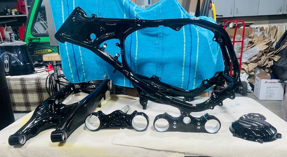 A glossy black motorcycle frame and various components, including the swingarm and triple tree, arranged on a workbench.