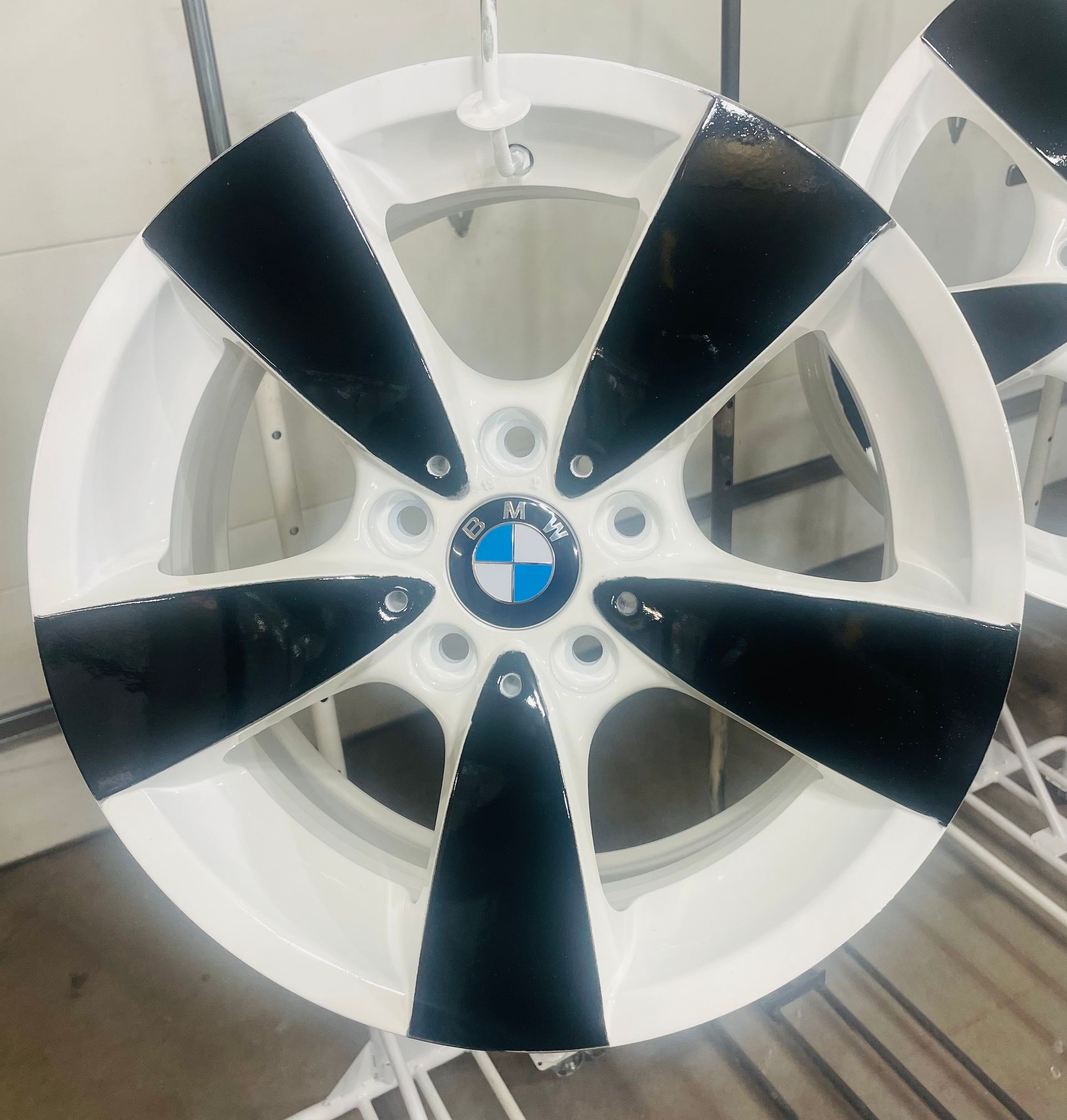 Two motorcycle wheels, light gray, hang in a garage. Tools and car are in the background.