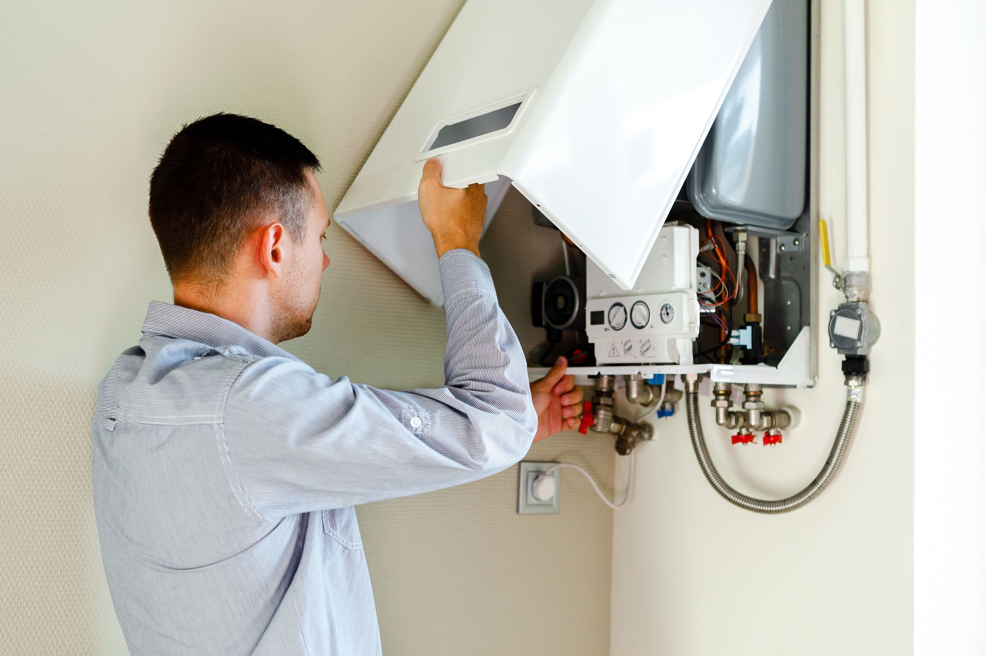 Man inspecting a white wall-mounted boiler, opening the access panel.