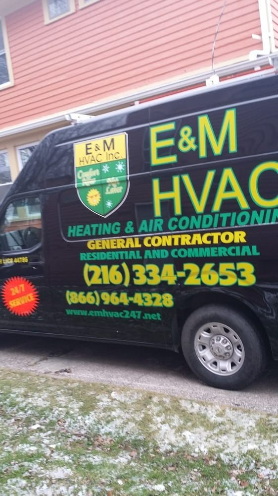 Black E&M HVAC van with green and yellow logo parked in front of a house. Contact info on the side.