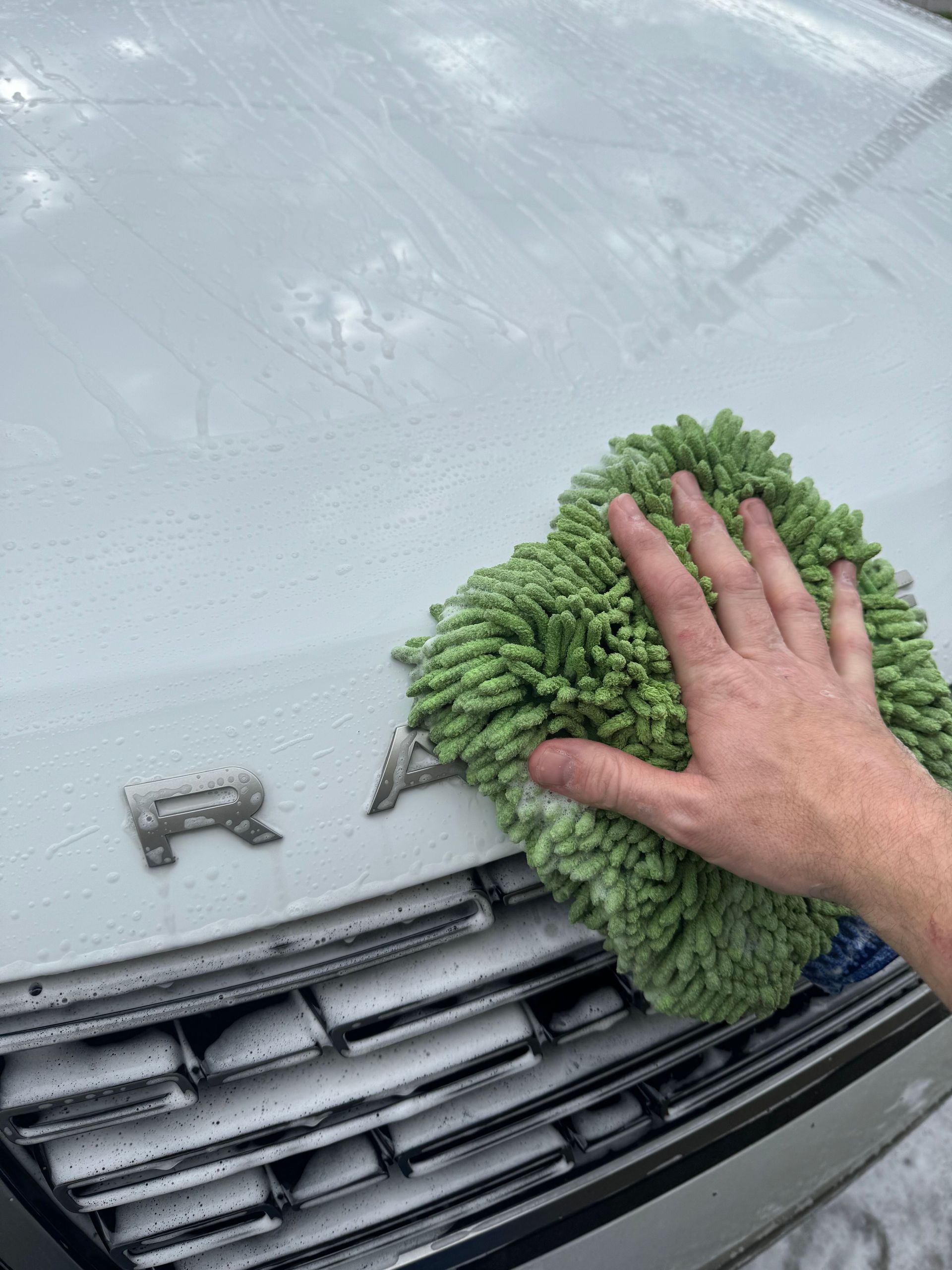 A person is cleaning the hood of a car with a green towel.