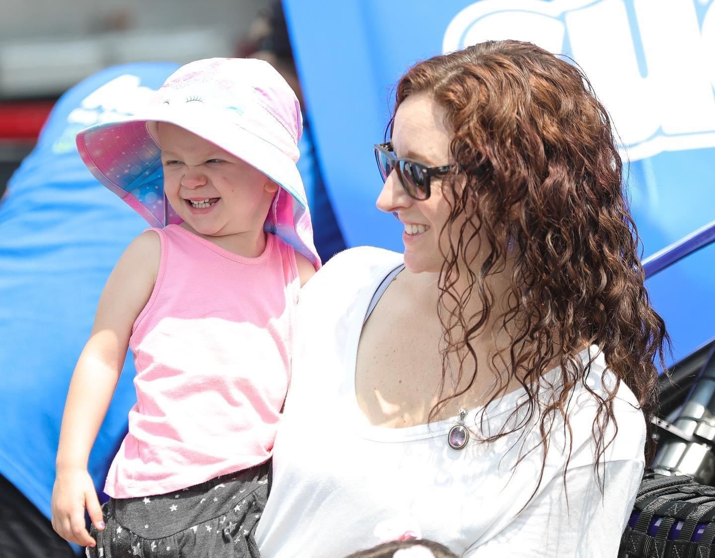 A woman is holding a little girl who is wearing a pink hat