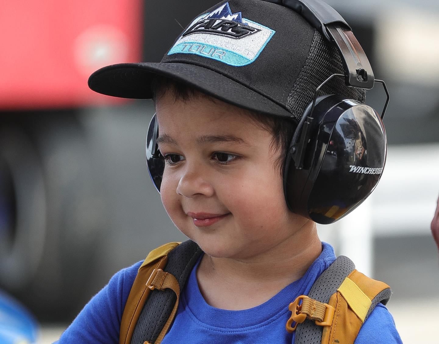 A young boy wearing a hat and headphones is smiling