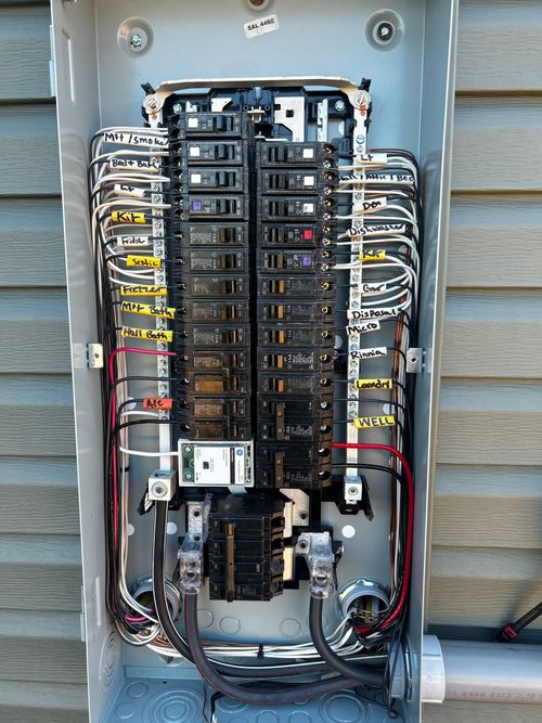 Open electrical panel with black breakers, wires, and gray box mounted.