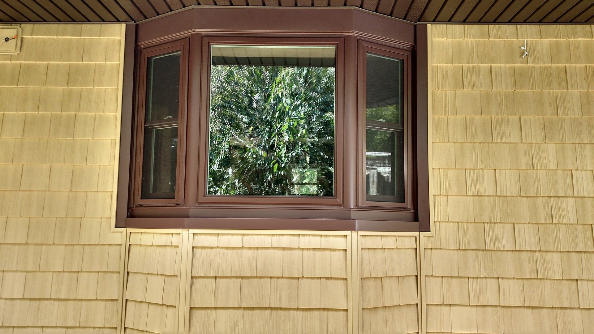 Bay window with brown trim, set in a yellow shingled exterior wall.