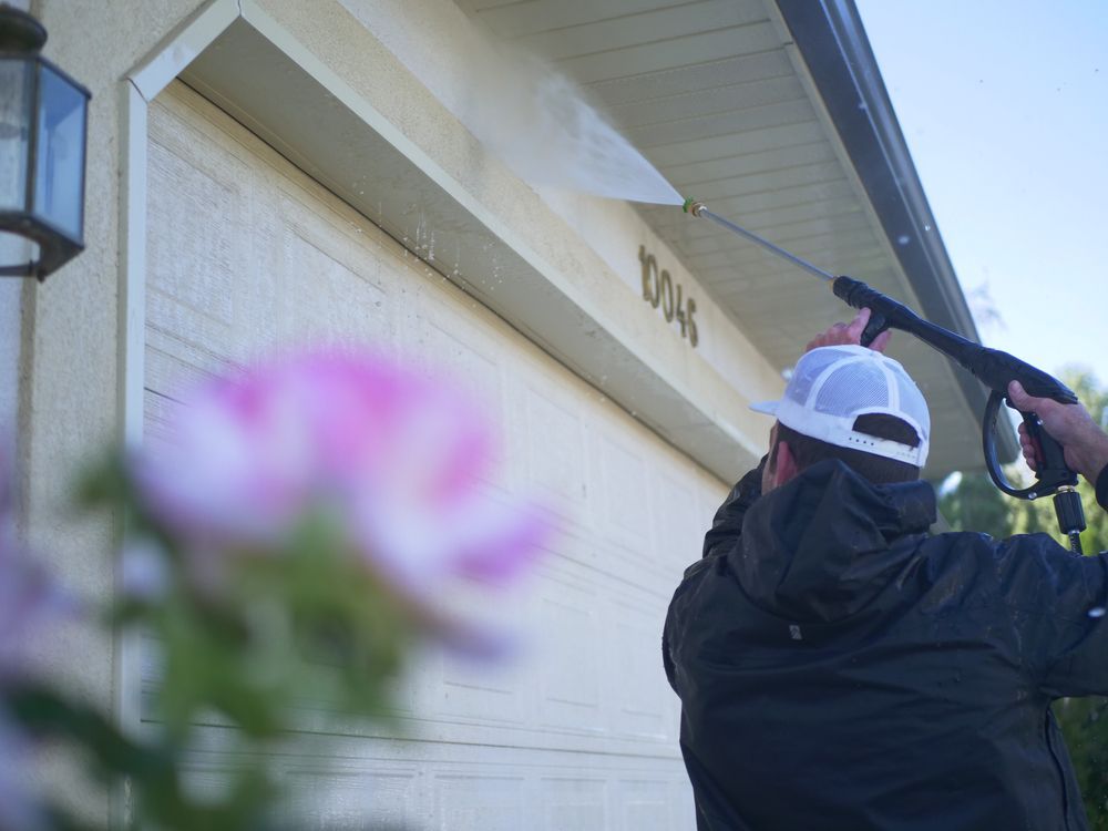 A Man Is Cleaning A Garage Door With A Pressure Washer — Jervis Bay Pressure Washing & Property Maintenance In Bomaderry, NSW