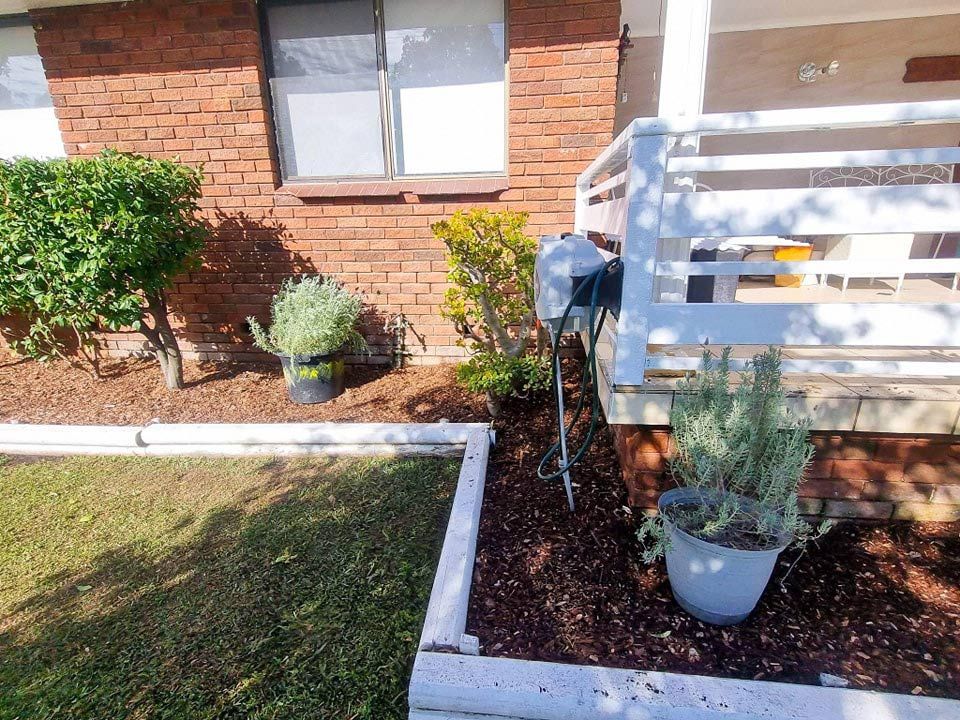 A Brick House With A White Railing And Potted Plants — Jervis Bay Pressure Washing & Property Maintenance in Culburra, NSW