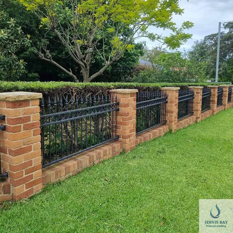 A Brick Fence With A Black Wrought Iron Fence — Jervis Bay Pressure Washing & Property Maintenance in Culburra, NSW