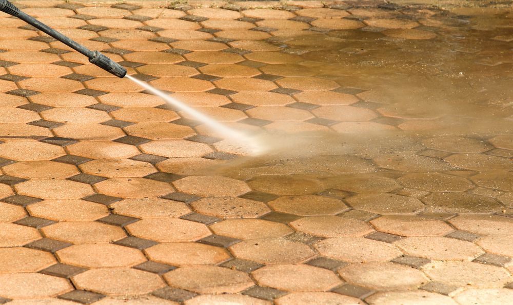 A Person Is Using Pressure Washer To Clean A Brick Floor — Jervis Bay Pressure Washing & Property Maintenance In Bowral, NSW
