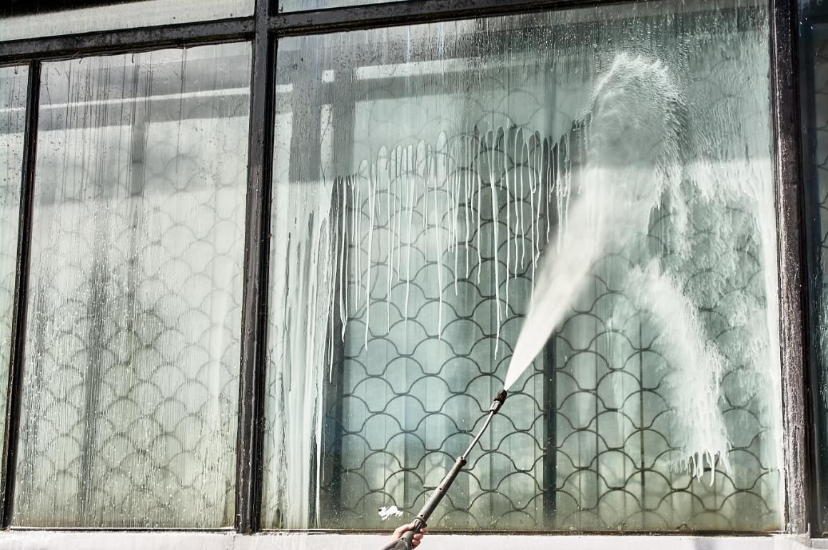 A Person Is Cleaning A Window With A High Pressure Washer — Jervis Bay Pressure Washing & Property Maintenance In Nowra, NSW