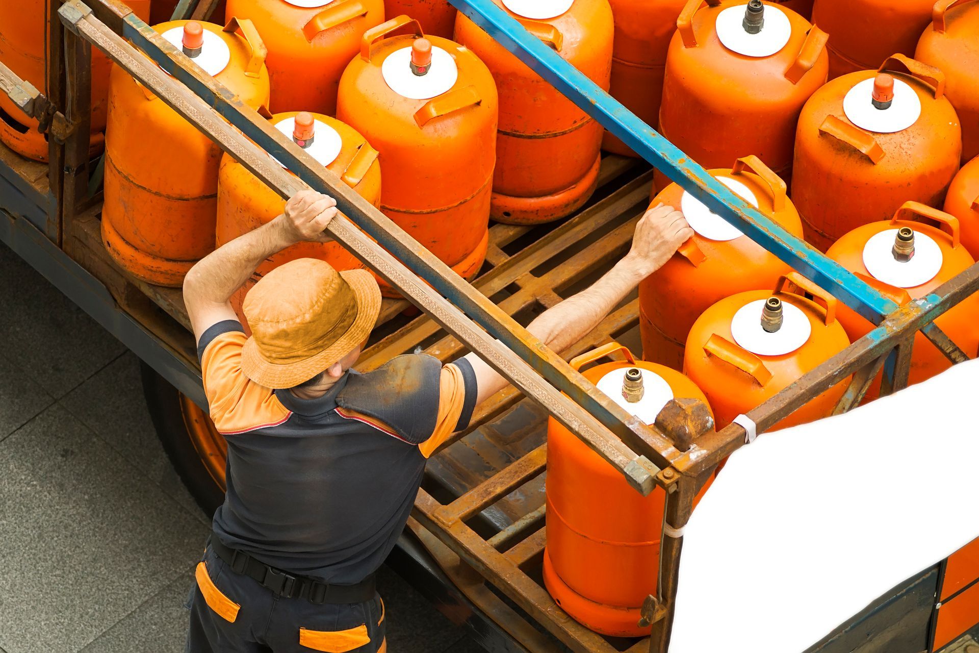 A man in a straw hat is loading orange gas cylinders into a truck
