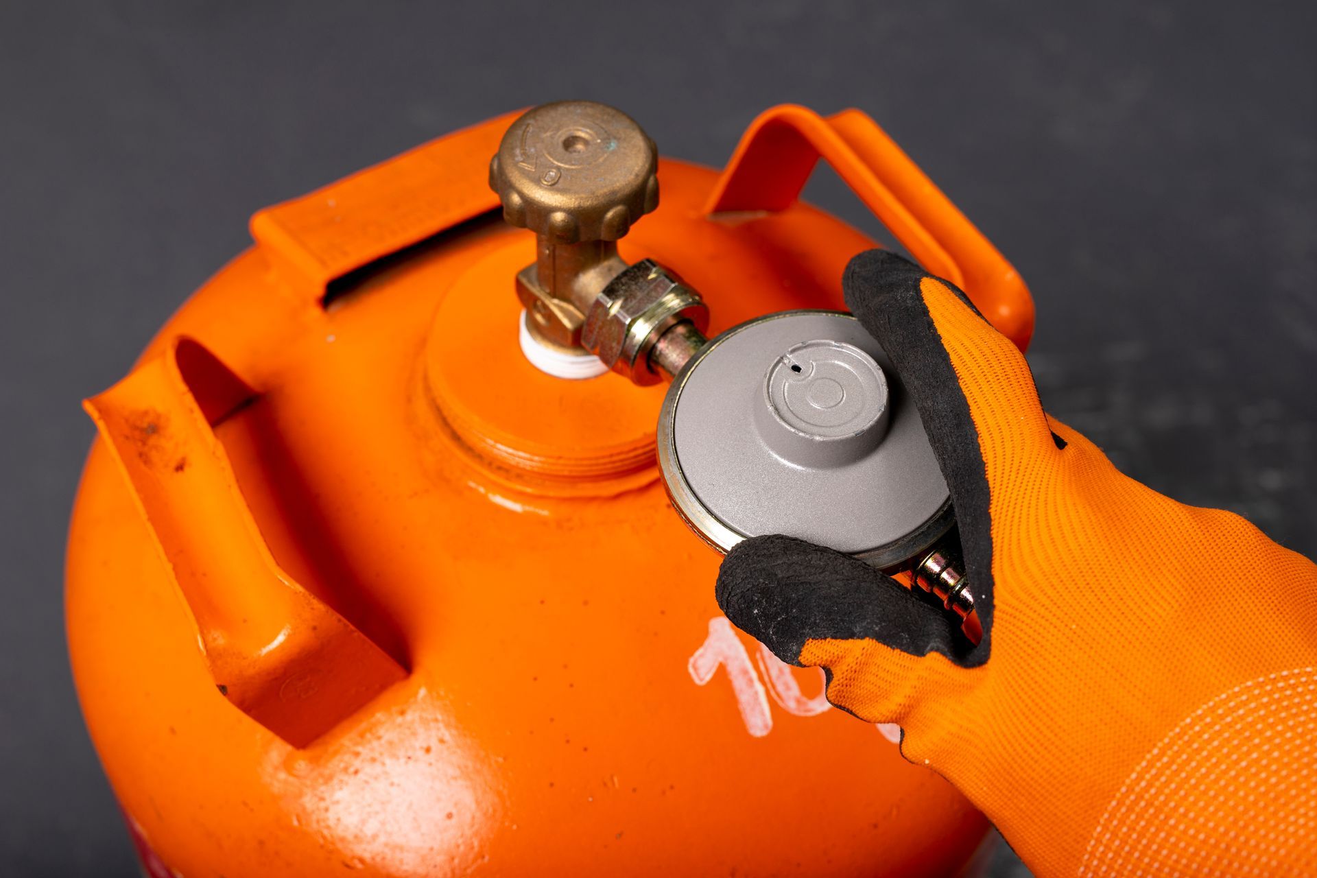 A person wearing orange gloves is holding a gas cylinder.