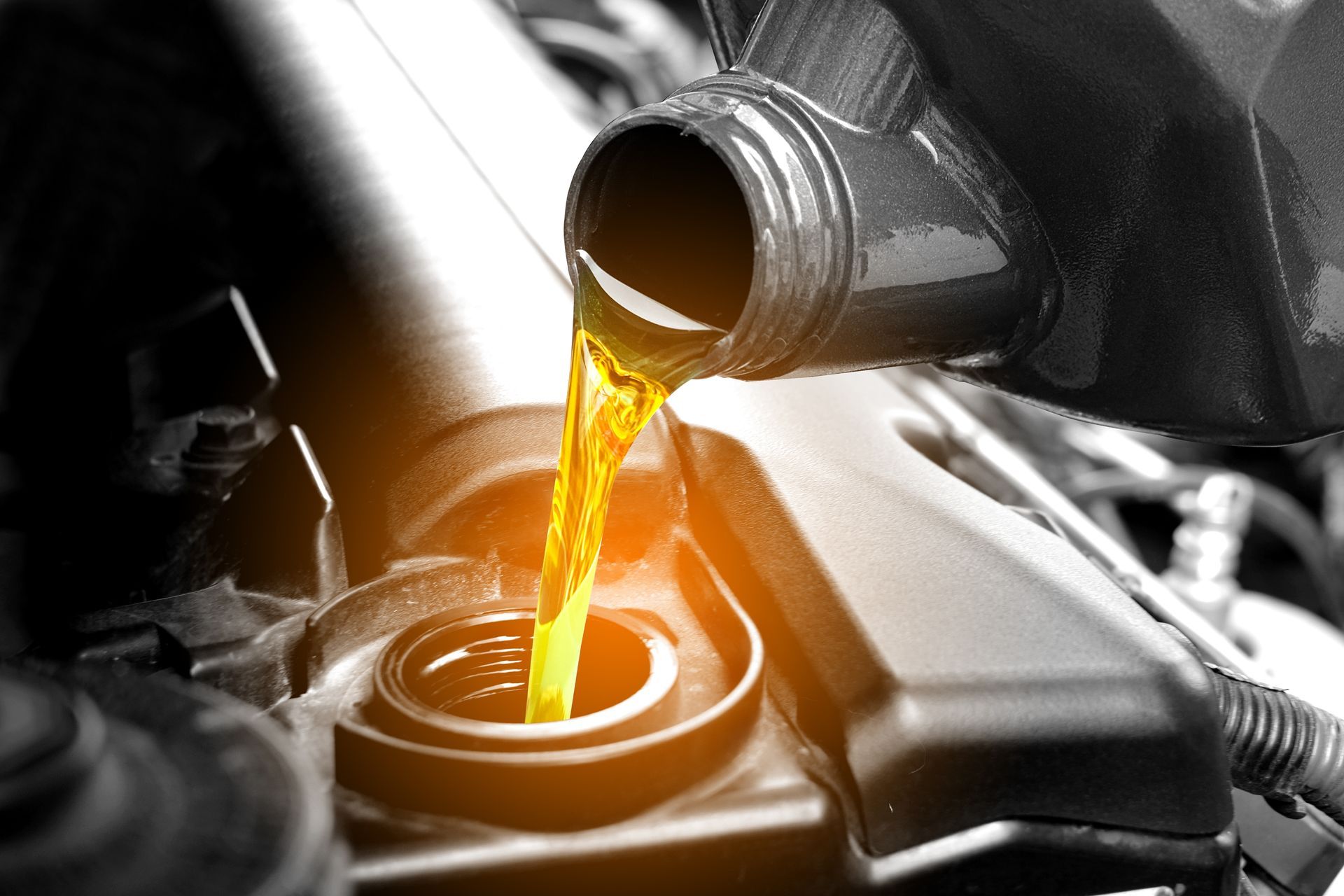 A close up of a person pouring oil into a car engine.