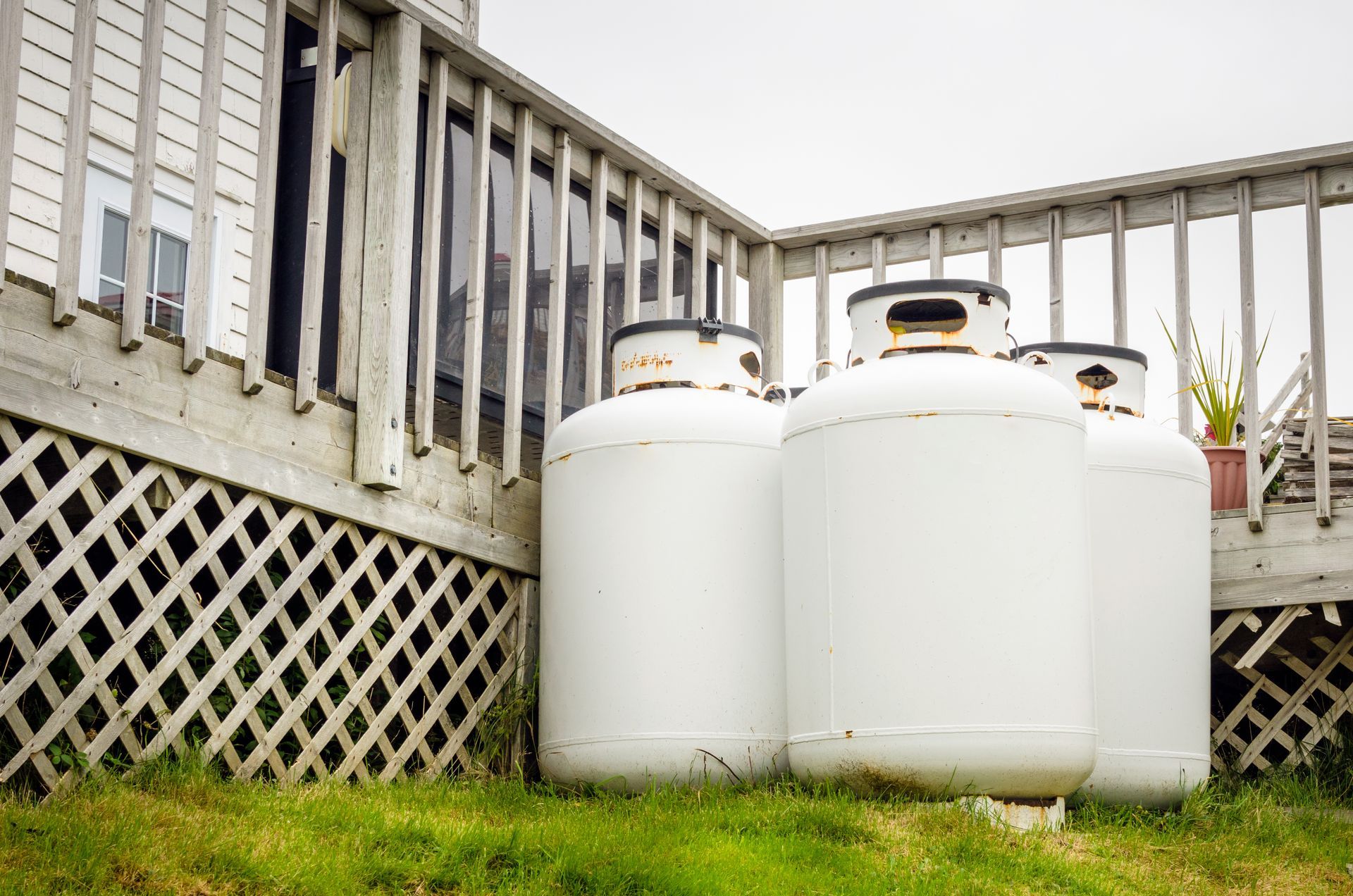 Three white propane tanks are sitting in the grass next to a deck.